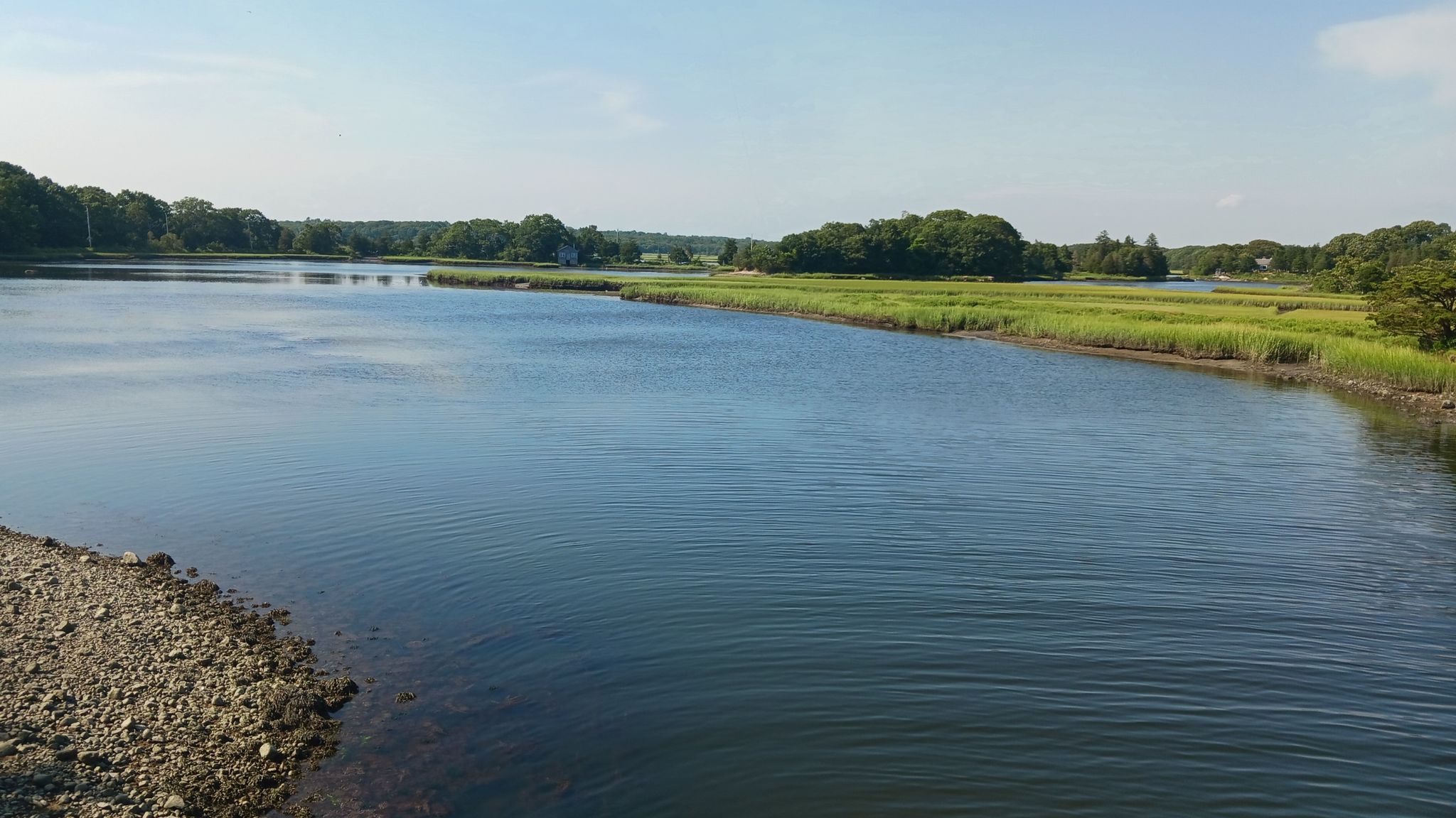Calm river flowing between green marshland and distant trees under a bright sky. - Apponagansett Beach – View of Westport Point loop from New Bedford