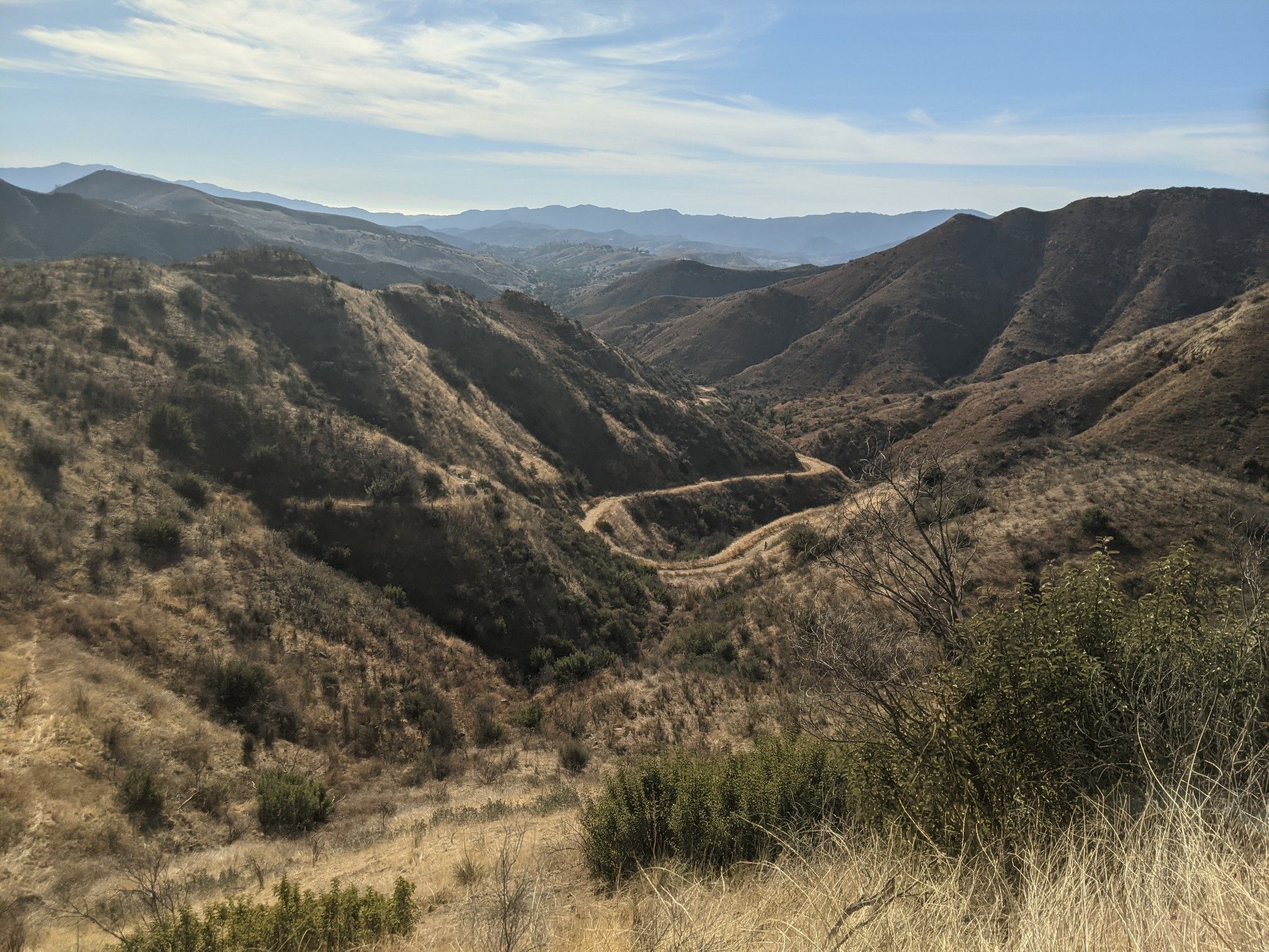 A winding dirt road through dry, brushy mountains under a partly cloudy sky. - Cheeseboro Canyon Trail – East Las Virgenes Canyon loop from Zev Yaroslavsky Las Virgenes Highlands Park