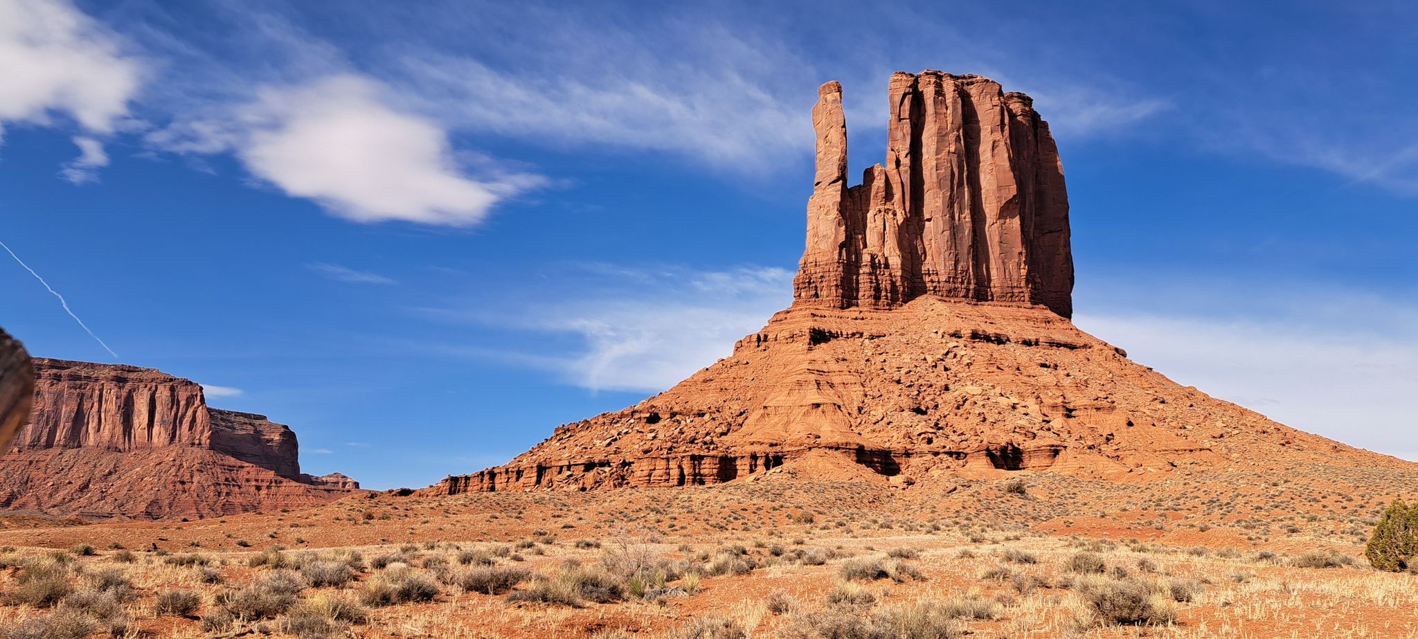 Large red rock formation under a bright blue sky with sparse desert plants. - Wildcat Trail
