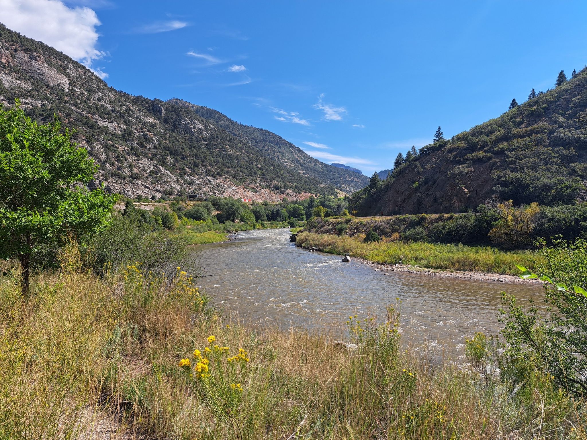 River winding through a valley with rocky, green mountains under a clear blue sky. - Glenwood Canyon Trail