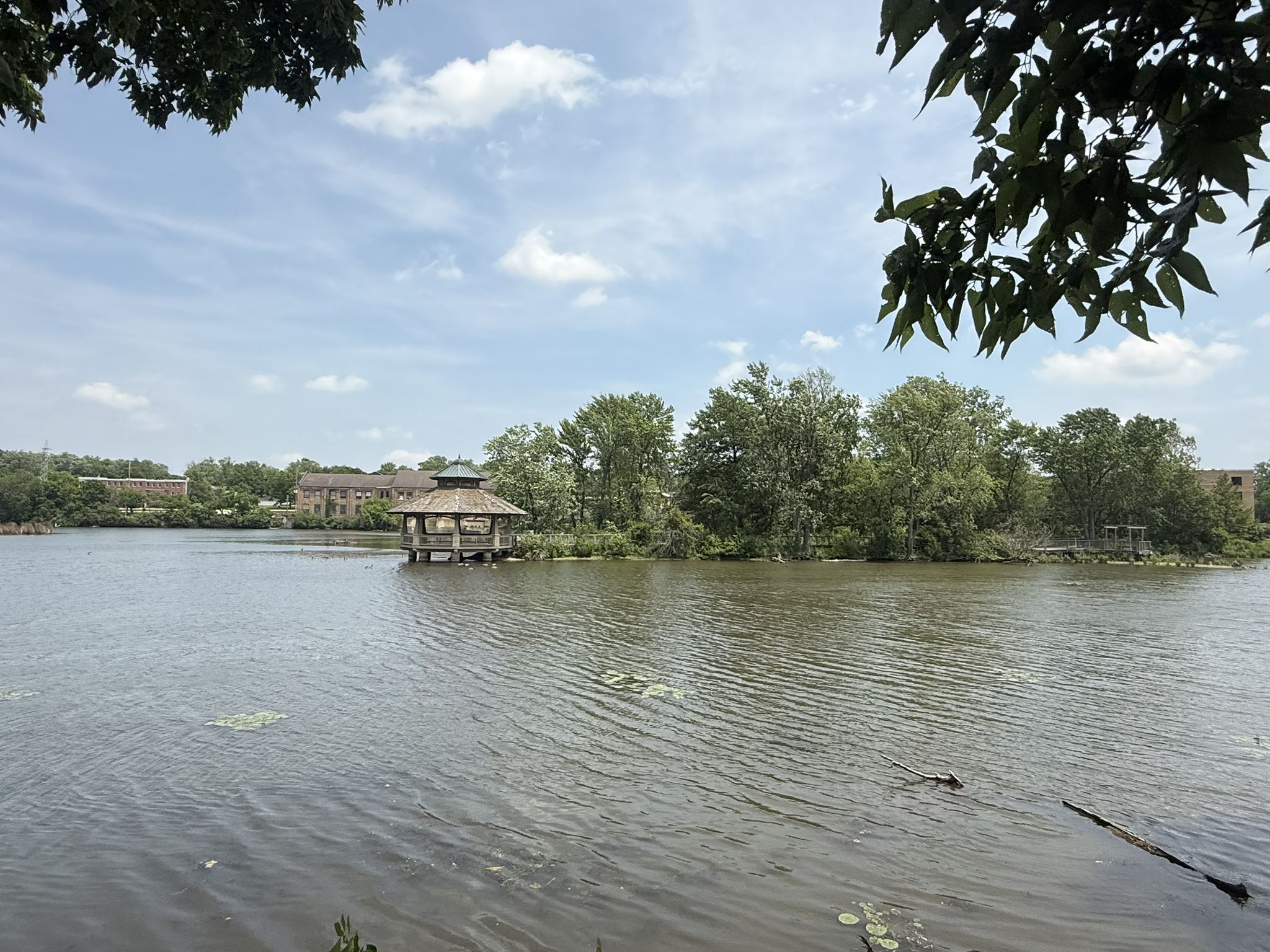 Lake with a wooden gazebo on stilts, surrounded by trees under a bright sky. - Batavia Depot Museum – "Children playing" statue loop from Batavia