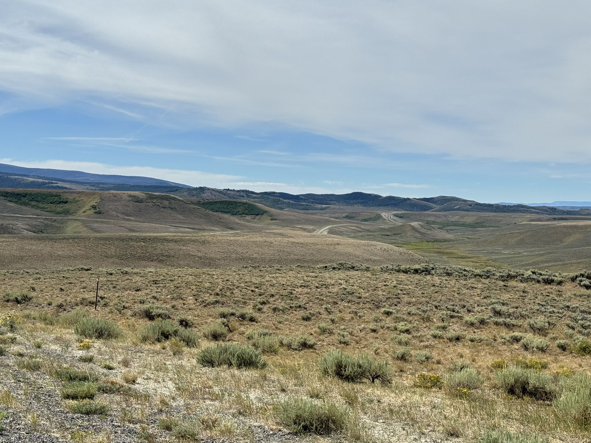 Vast dry, rolling landscape with distant hills under a hazy blue sky. - Sage Creek Road to Sage Creek Cliffs Overlook