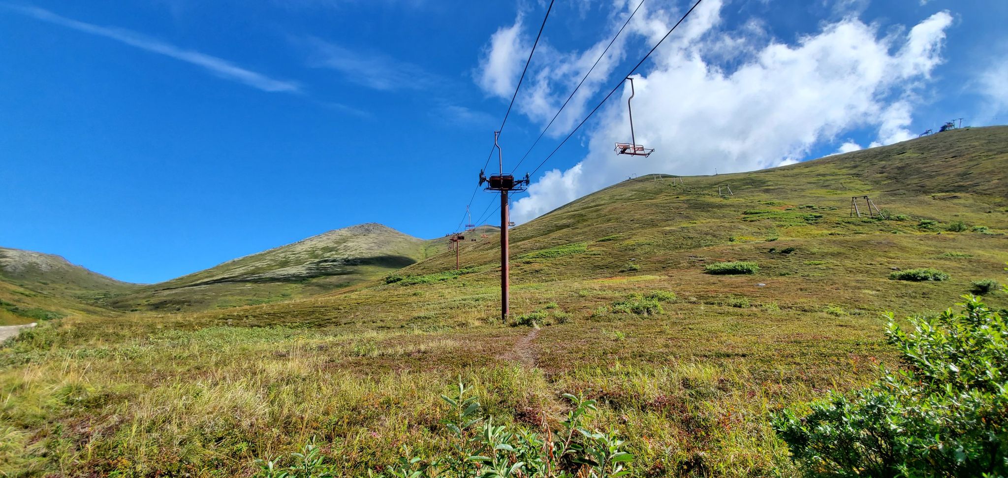 Ski lift chairs and tower against green hills under a bright blue sky. - Rendezvous Peak and Mount Gordon Lyon Loop