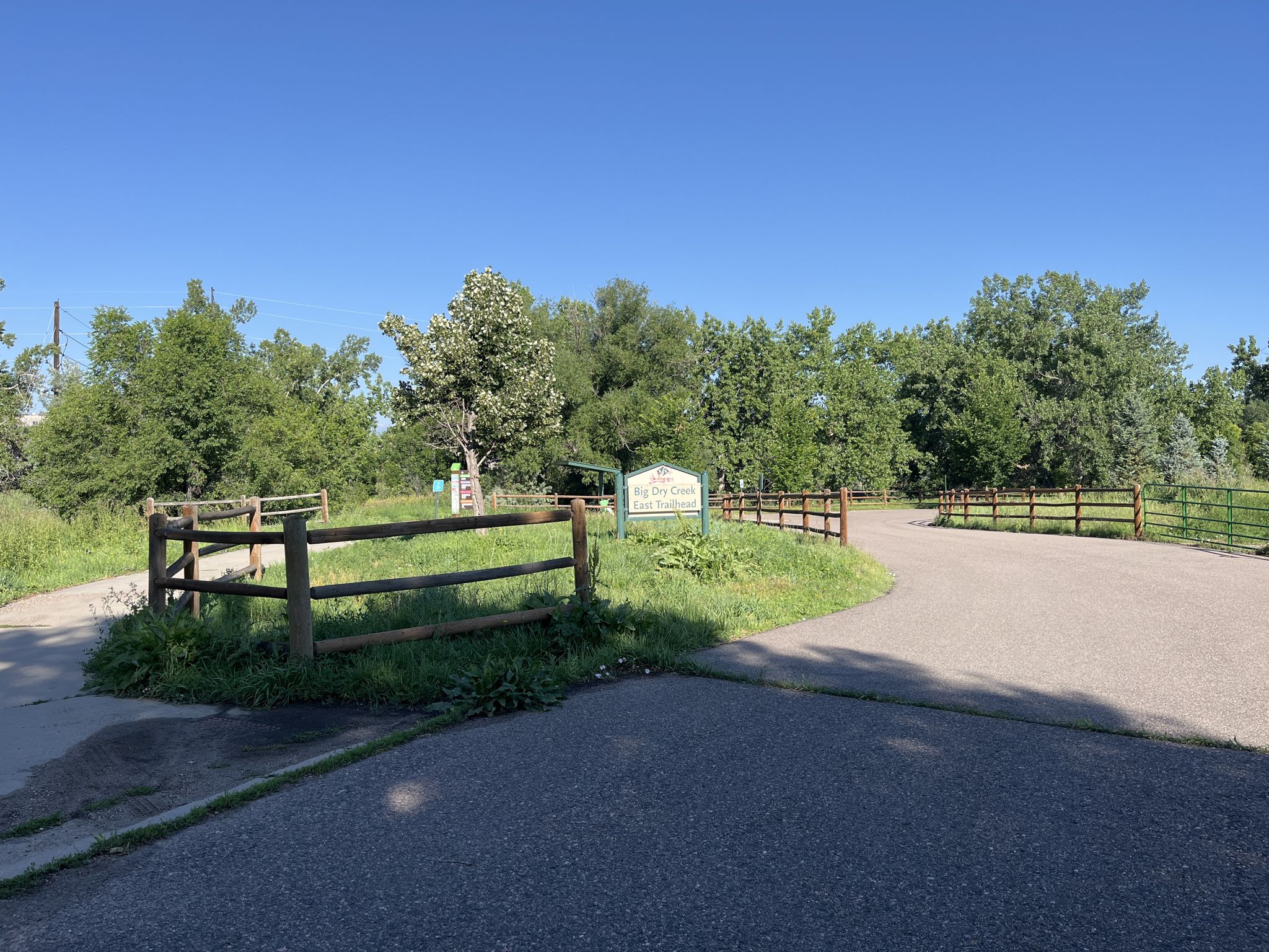 Paved and dirt paths diverge near a wooden fence and green trees. - Roadbike loop from Greenwood Village