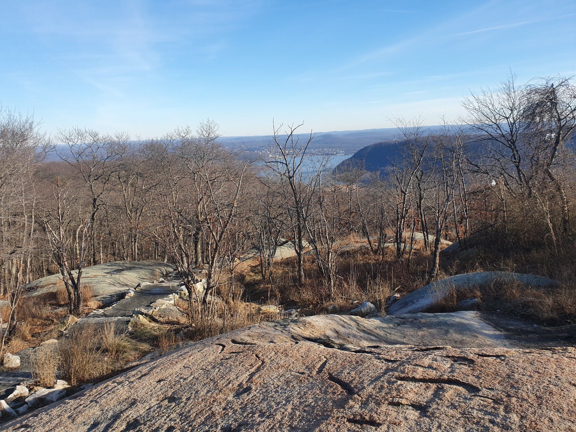Rocky terrain and bare trees frame a distant river in a valley under a clear sky. - Bear Mountain Loop via Major Welch and Appalachian Trail