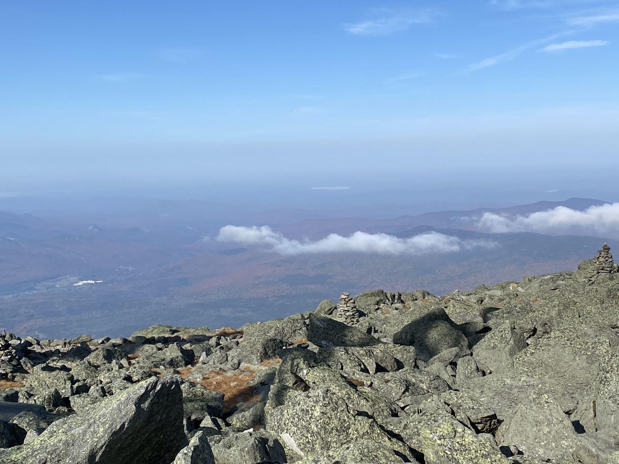 Rocky mountain summit with cairns overlooking a vast, cloudy landscape under blue sky. - Crawford Path