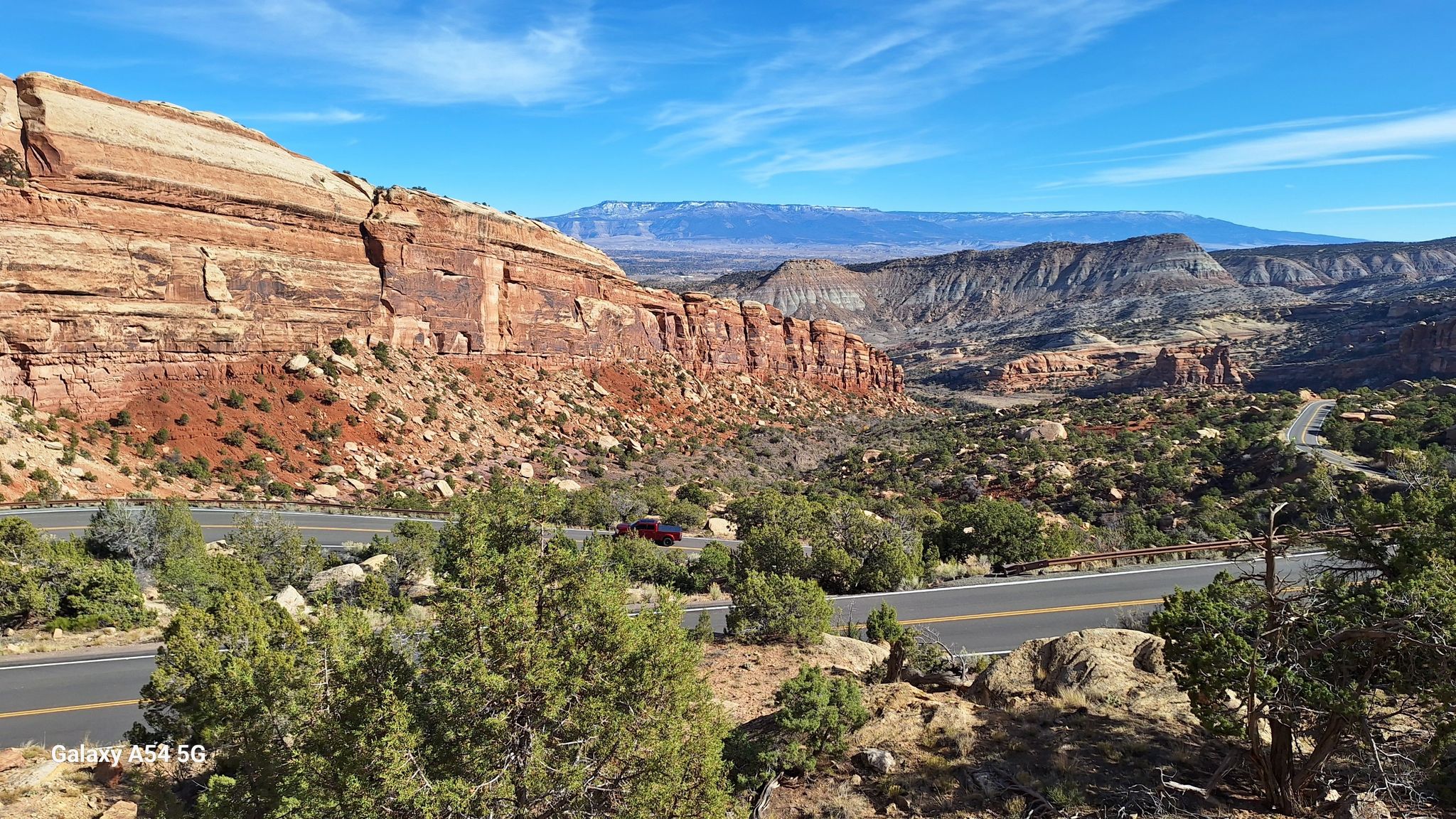 Scenic road next to a massive red rock cliff under a blue sky. - Glade Park to Little Park loop