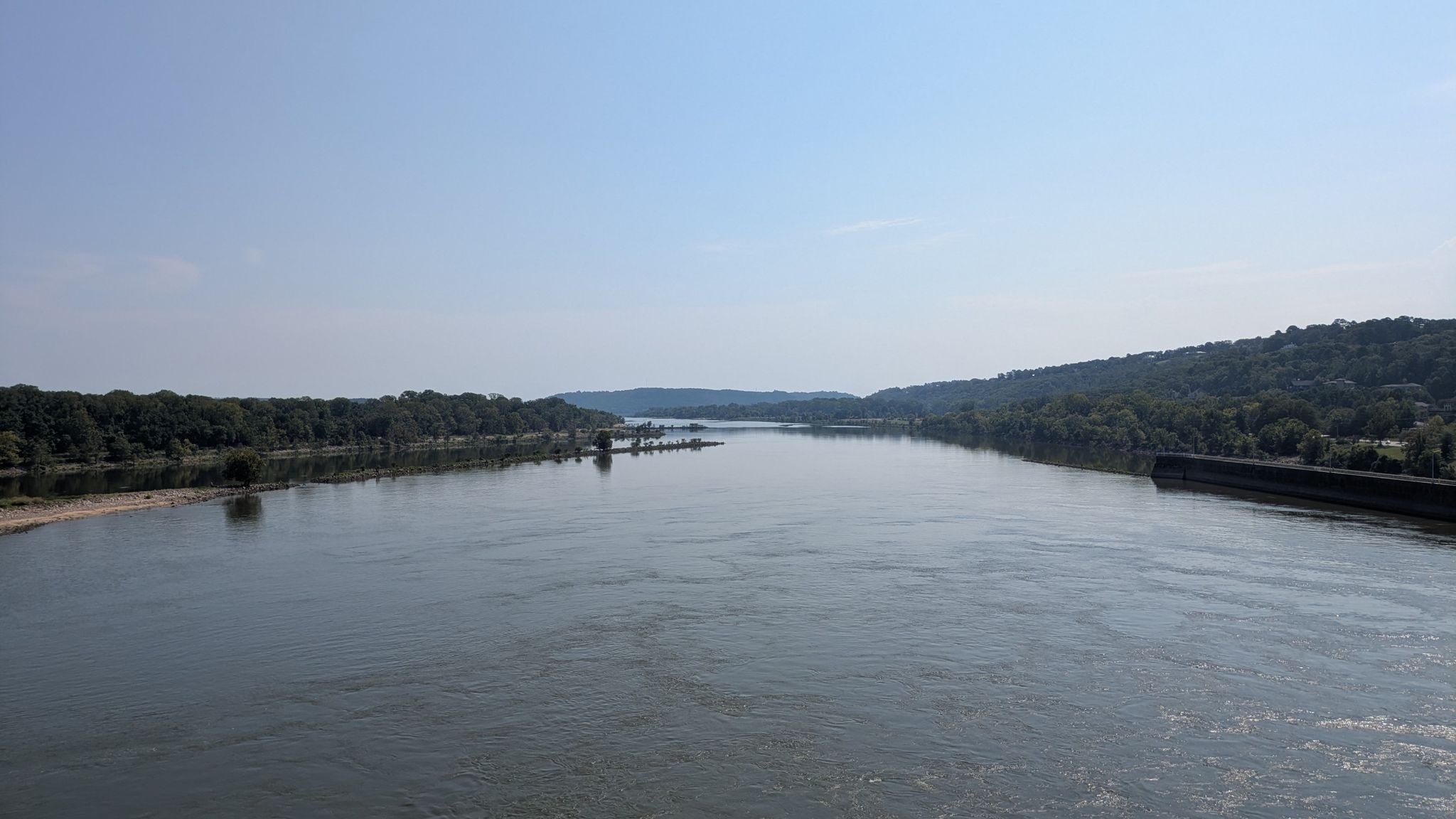 Wide river flows between forested banks under a clear blue sky. - Big Dam Bridge – Arkansas River Trail loop from Rodney Parham Rd & AR Valley Dr