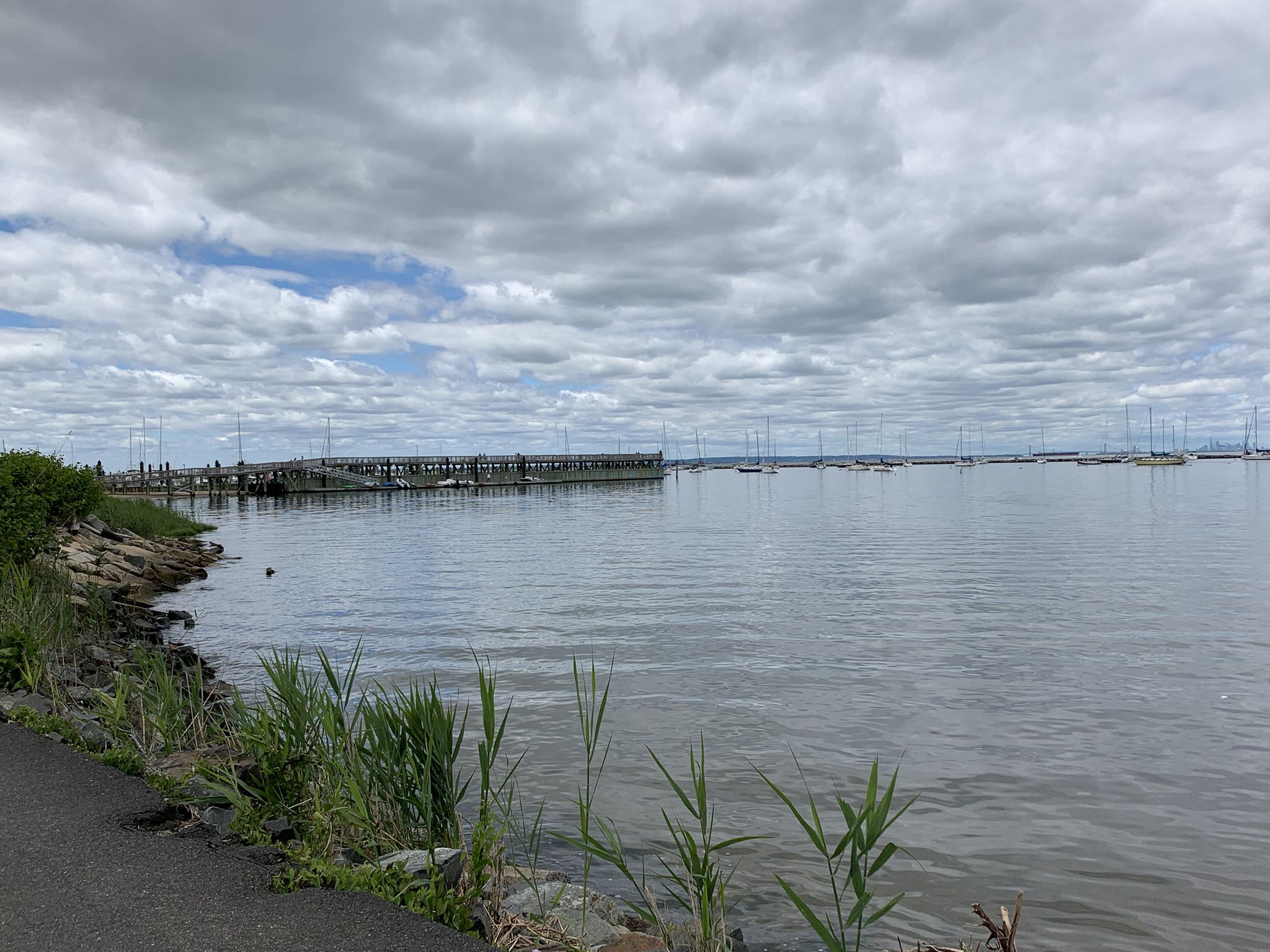 Cloudy day over a wide bay with a long pier and distant boats. - Henry Hudson Trail