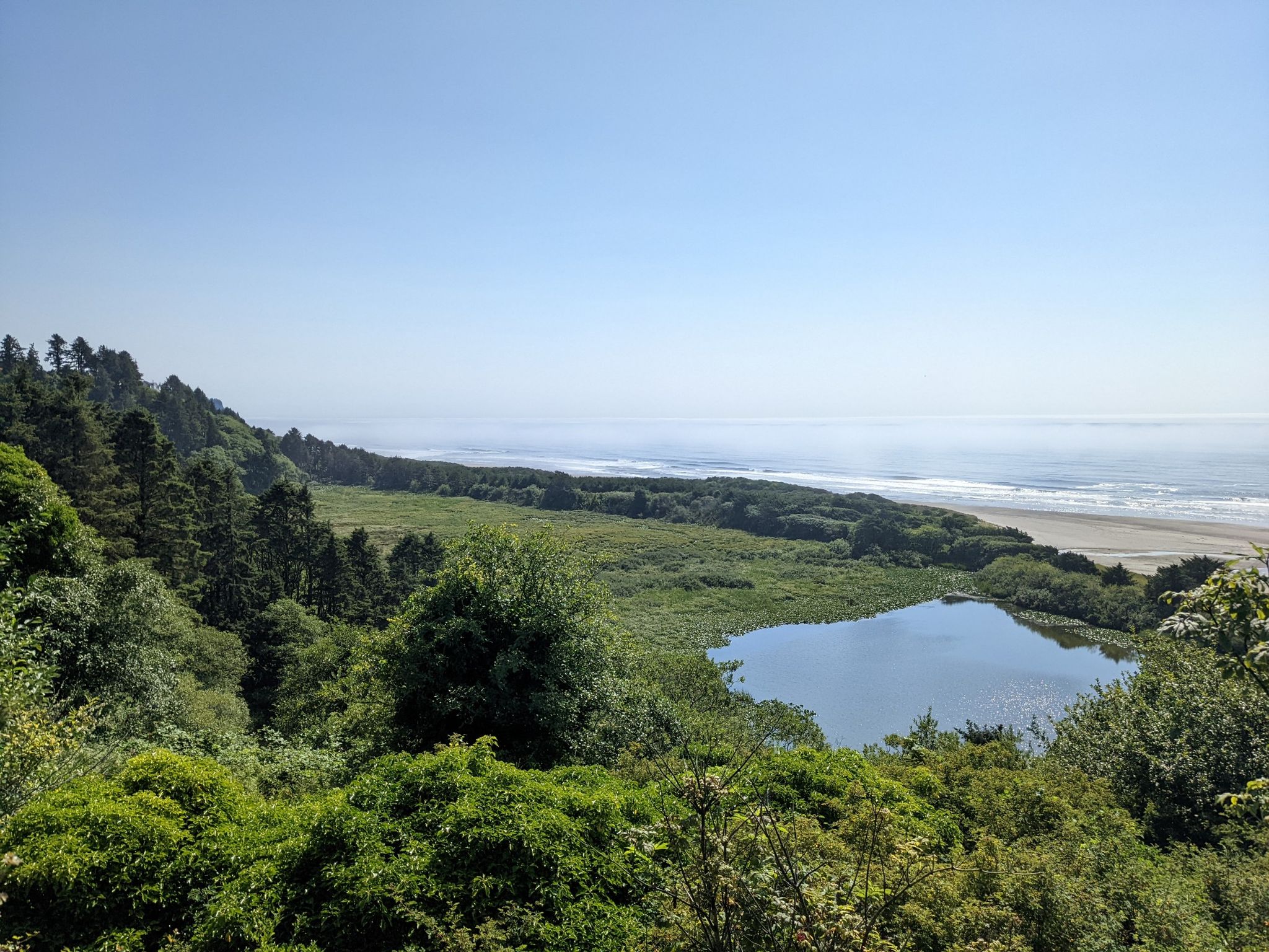 Sunny coastal view of ocean, sandy beach, calm lake, and green forest. - Pacific City – Winema Beach Viewpoint loop from Pacific City