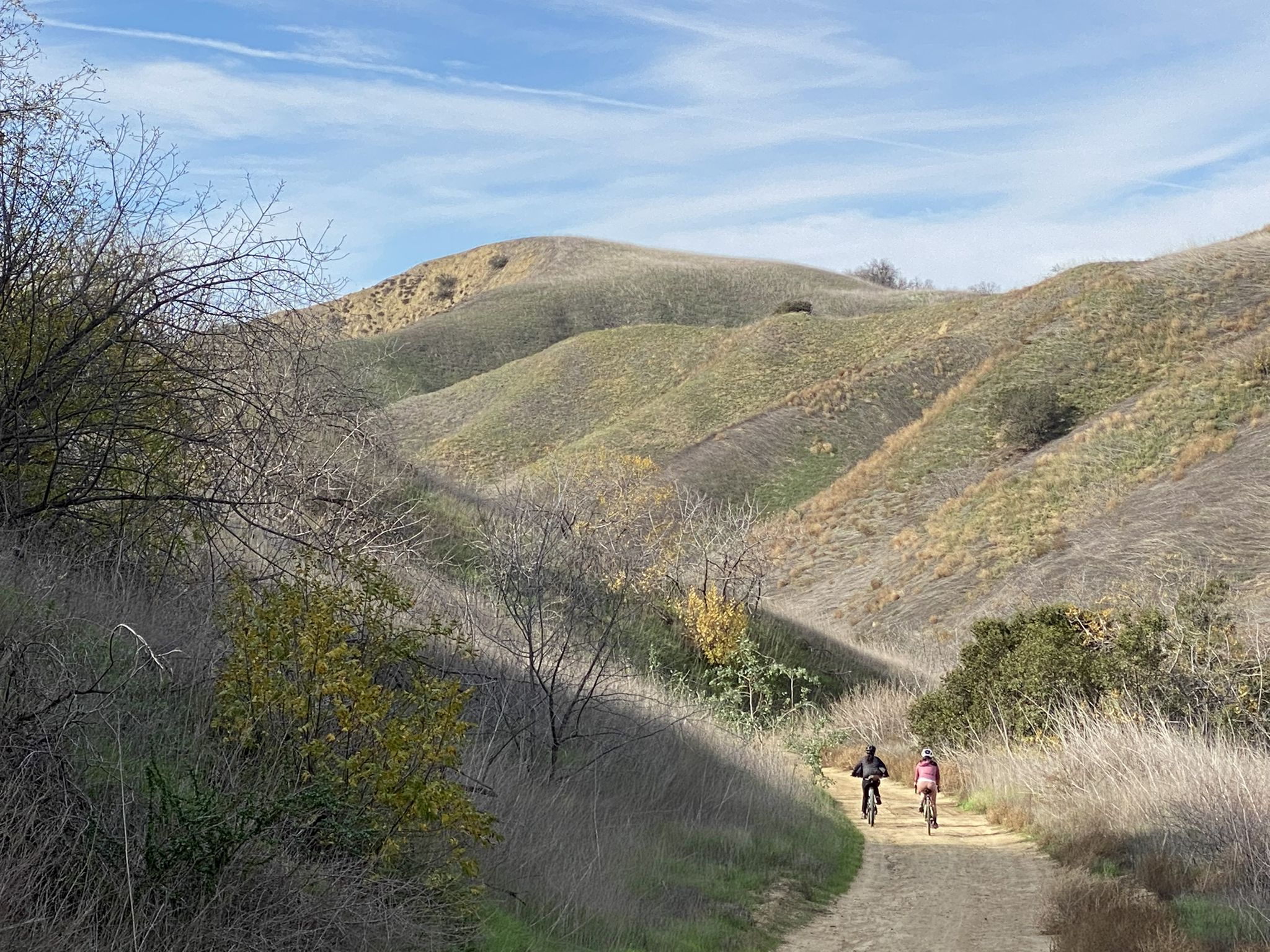 Two people mountain biking on a dirt path through rolling, grassy hills. - Telegraph Canyon Trail