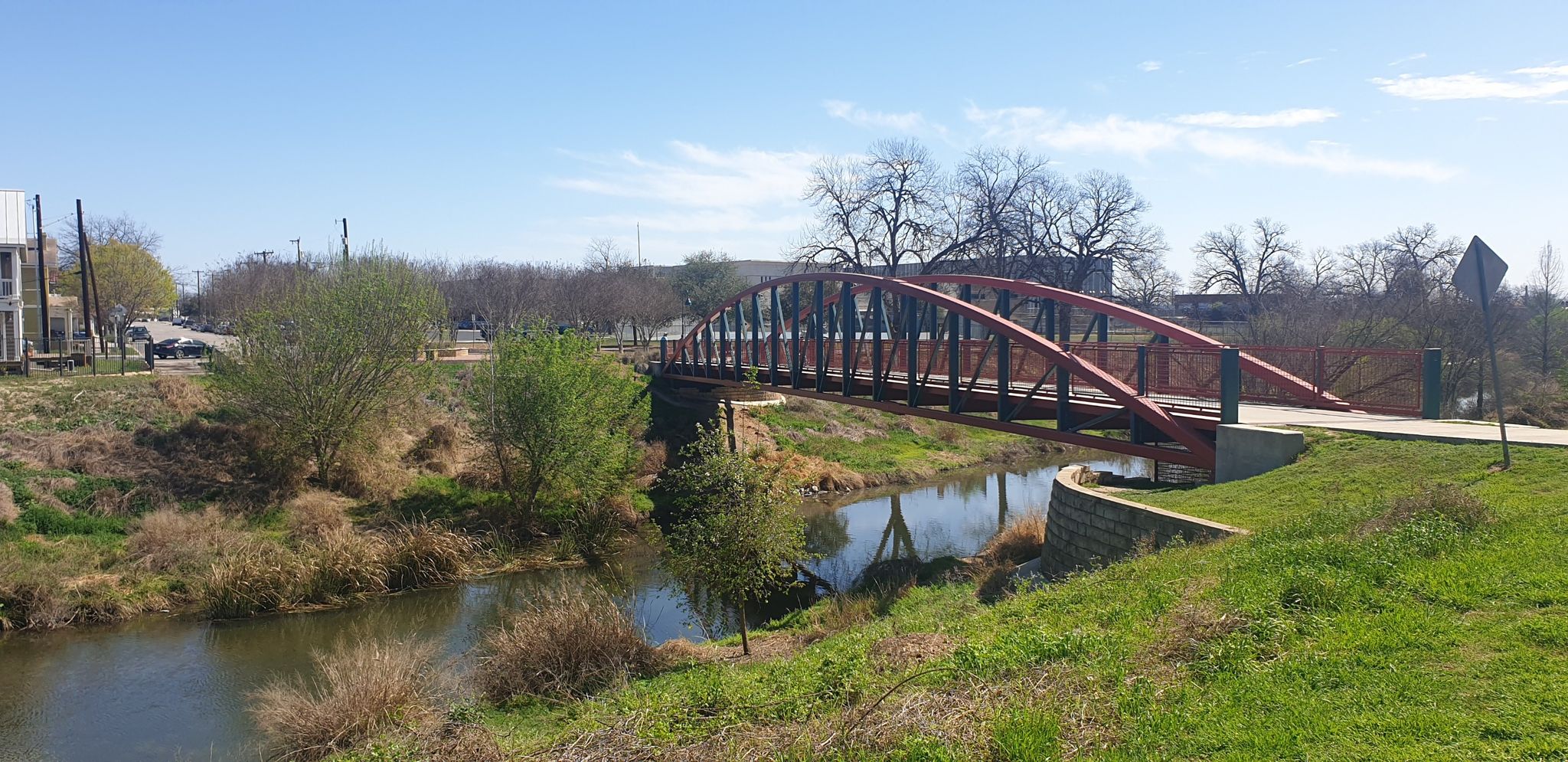 Red arched bridge over a narrow river with green banks, clear blue sky. - San Antonio River View loop from San Antonio