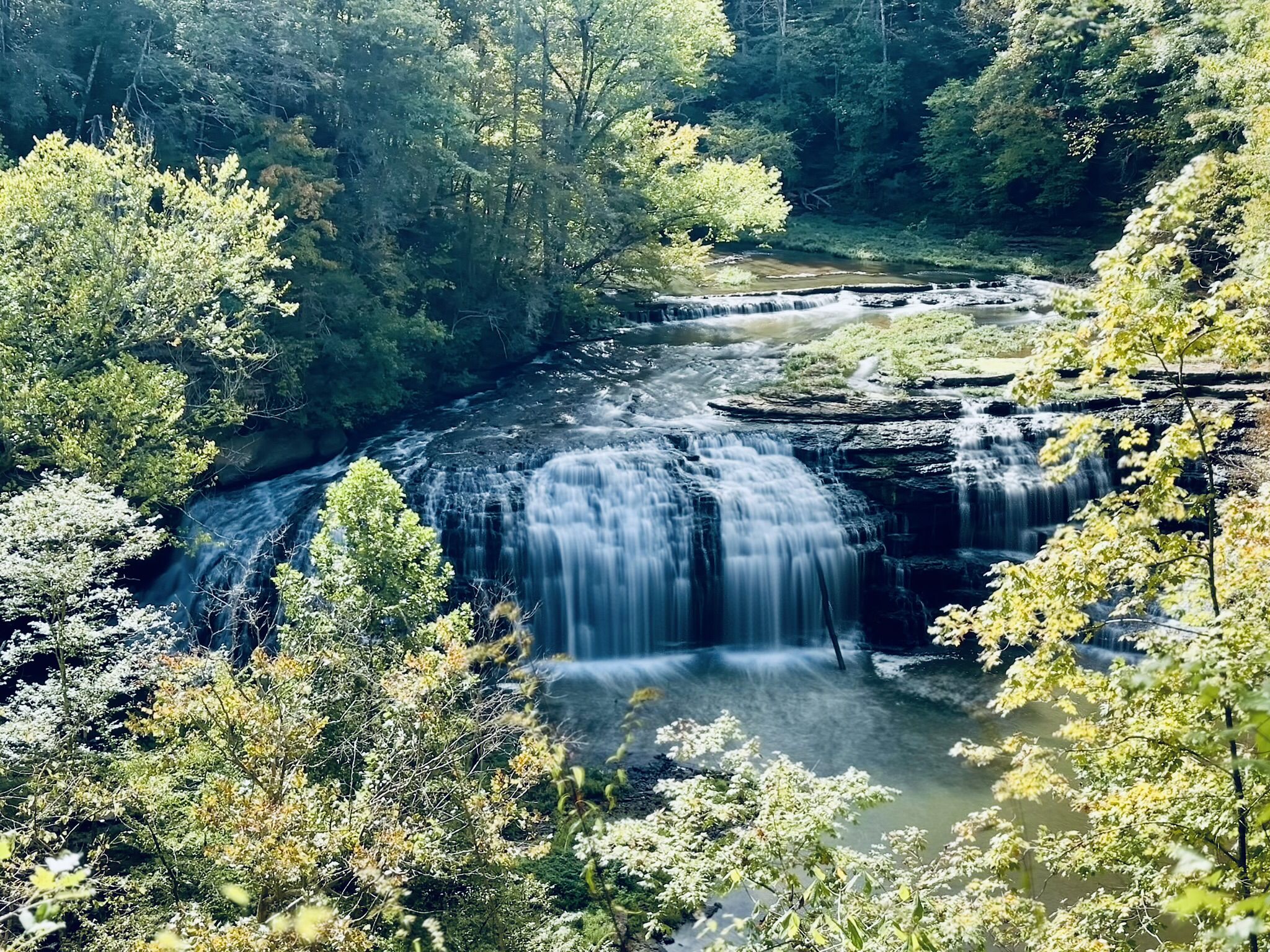 Cascading waterfall surrounded by lush green and autumn trees in bright daylight. - River and Ridgetop Trail Loop