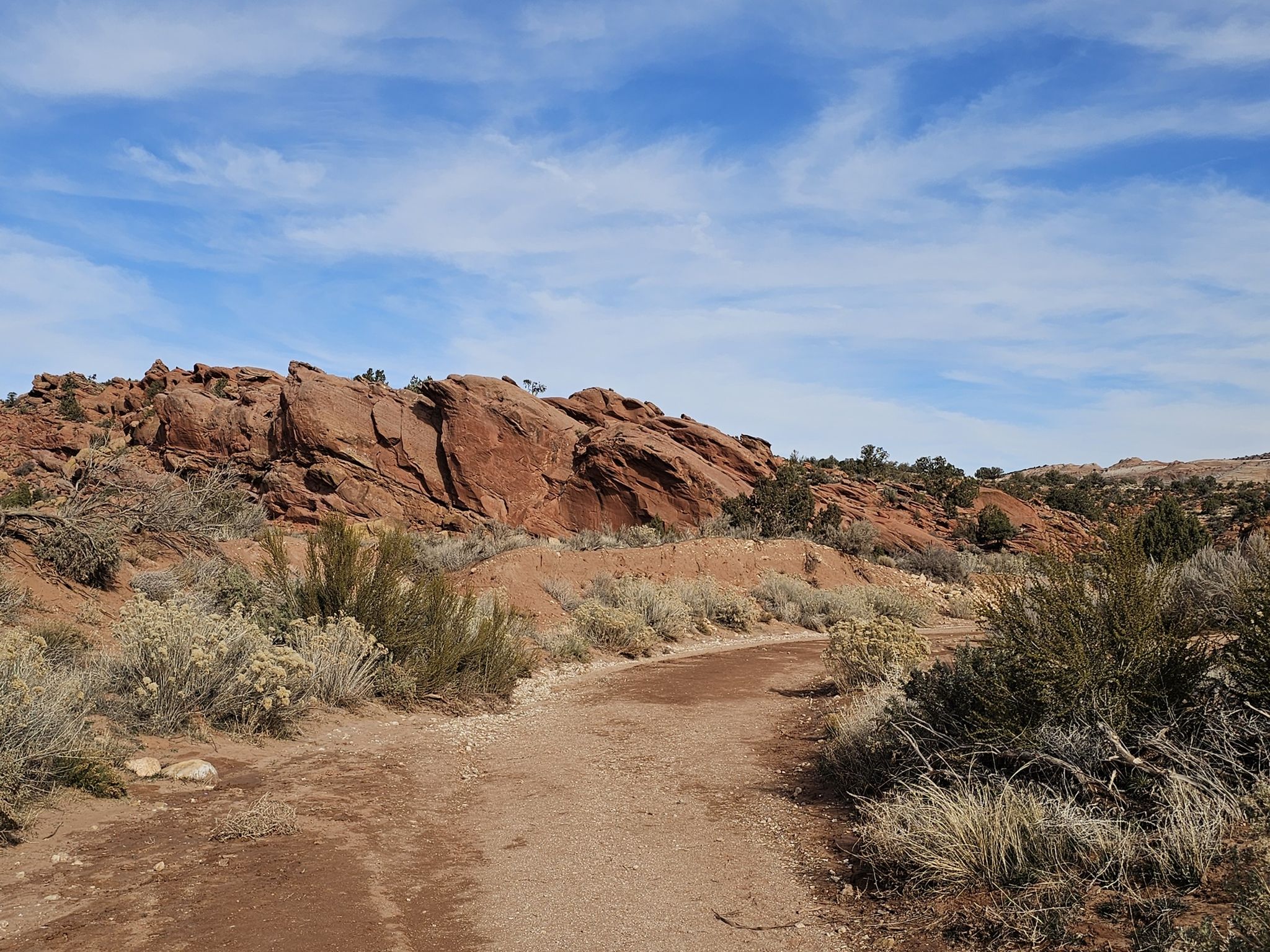 Dirt path through desert brush leading to red rock formations under blue sky. - Wire Pass to Buckskin Gulch Trail