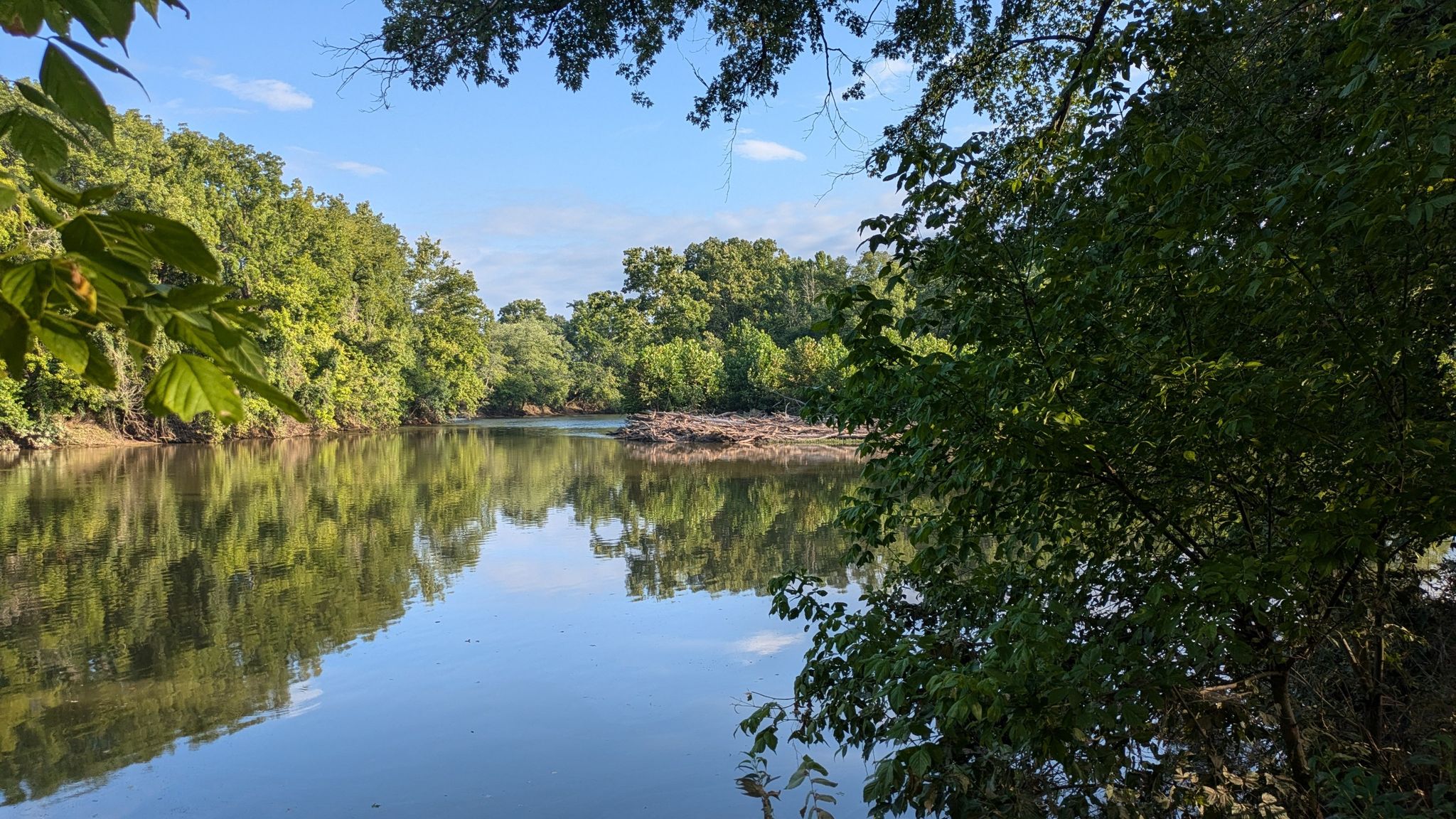 Calm water reflecting lush green trees under a bright blue sky. - Cool Spring Battlefield – View of the Shenandoah Valley loop from Shenandoah Retreat