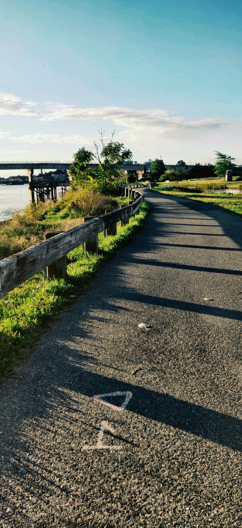 Paved path with wooden fence beside water under a sunny sky. - Mystic Link Trail