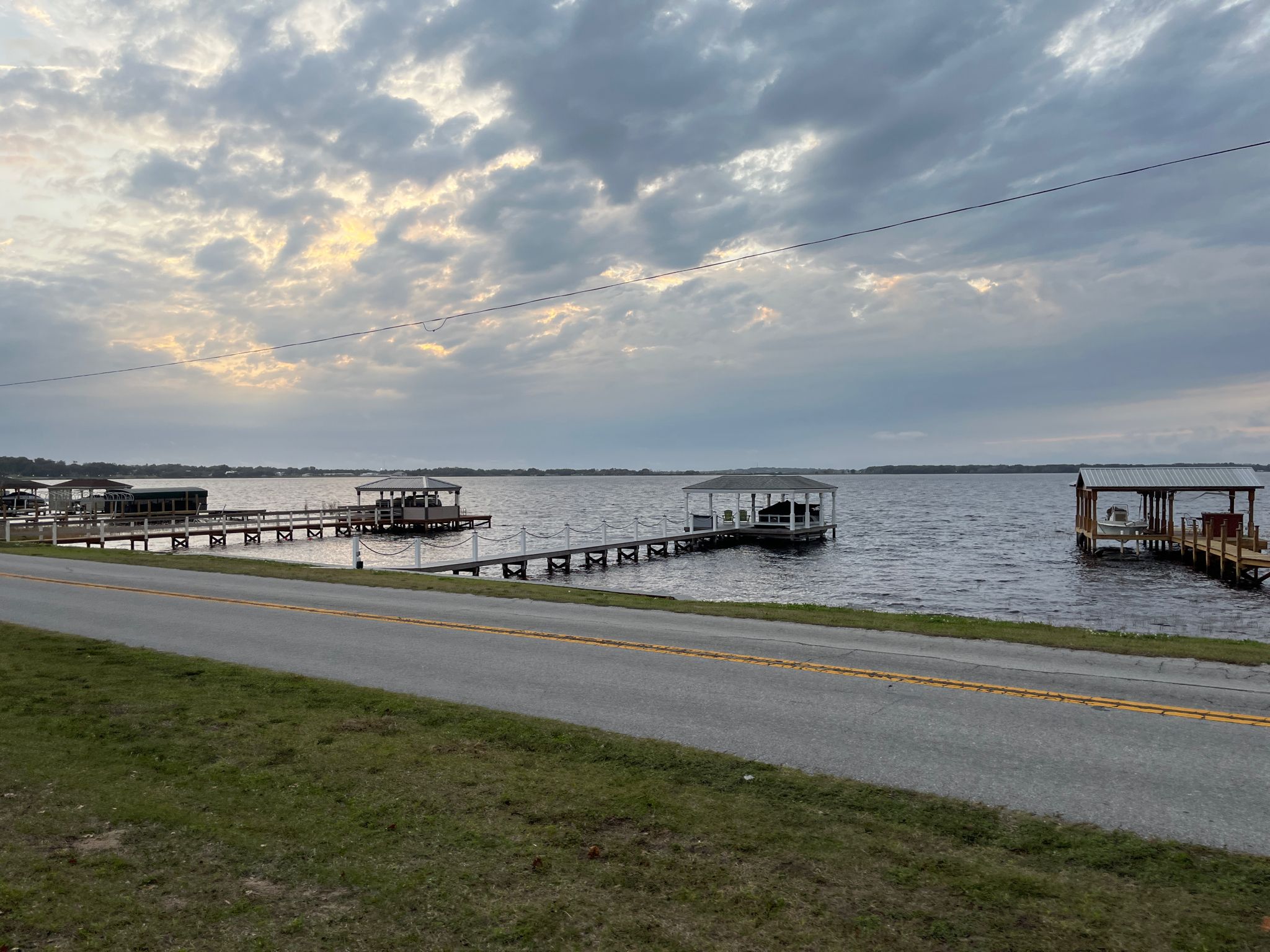 Overcast view of a lake with docks and a paved road in the foreground. - Epic Cycles – Lake Hiawatha Preserve loop from Clermont