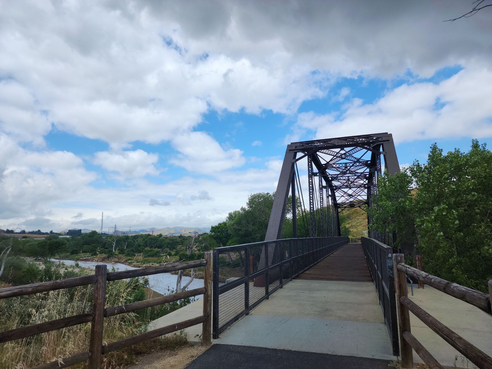 A metal truss bridge spans a river with green trees under a partly cloudy sky. - Iron Horse Bridge – San Francisquito Creek Trail loop from Saugus