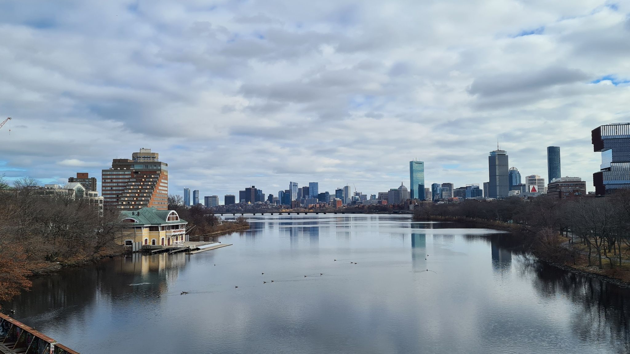 Wide river with a boathouse and distant city skyline under cloudy skies. - Arnold Arboretum to Bedford via Minuteman Bikeway