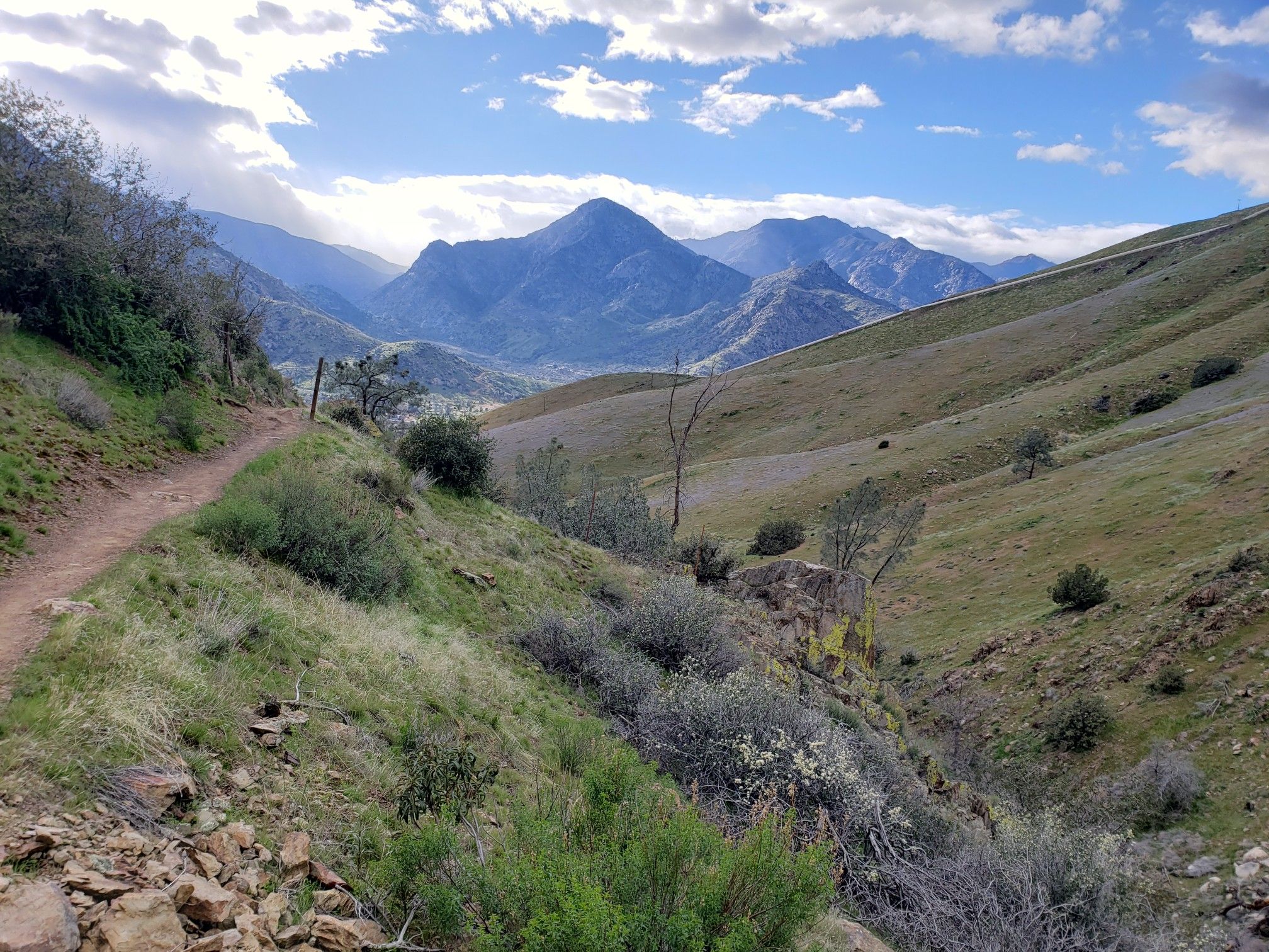 Dirt trail winding through green hills with distant mountains under a partly cloudy sky. - Cannell Trail loop from Camp Owens