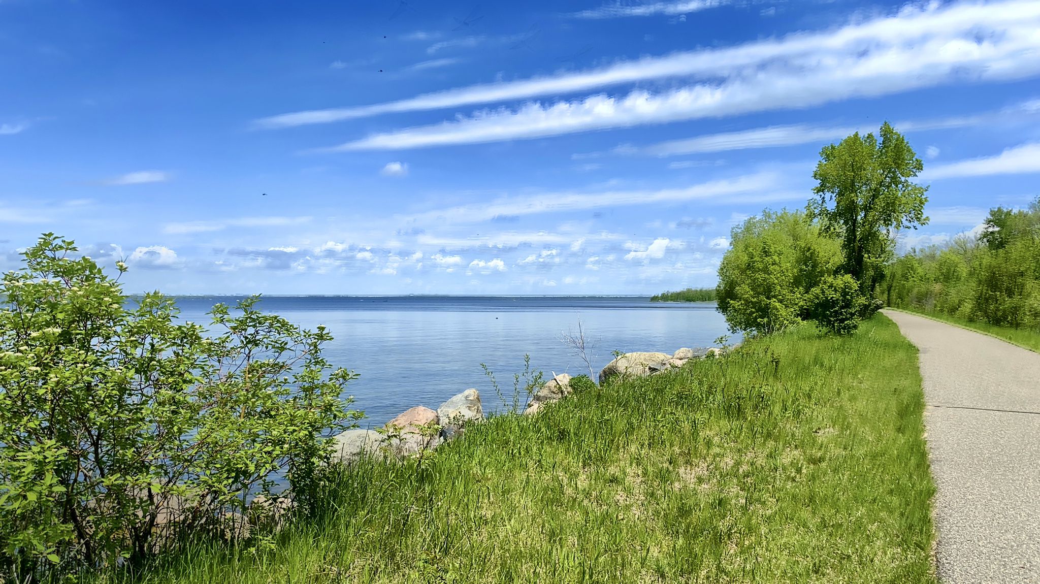 Paved path alongside a calm lake under a bright blue sky. - South Shore Beach loop from Lavinia