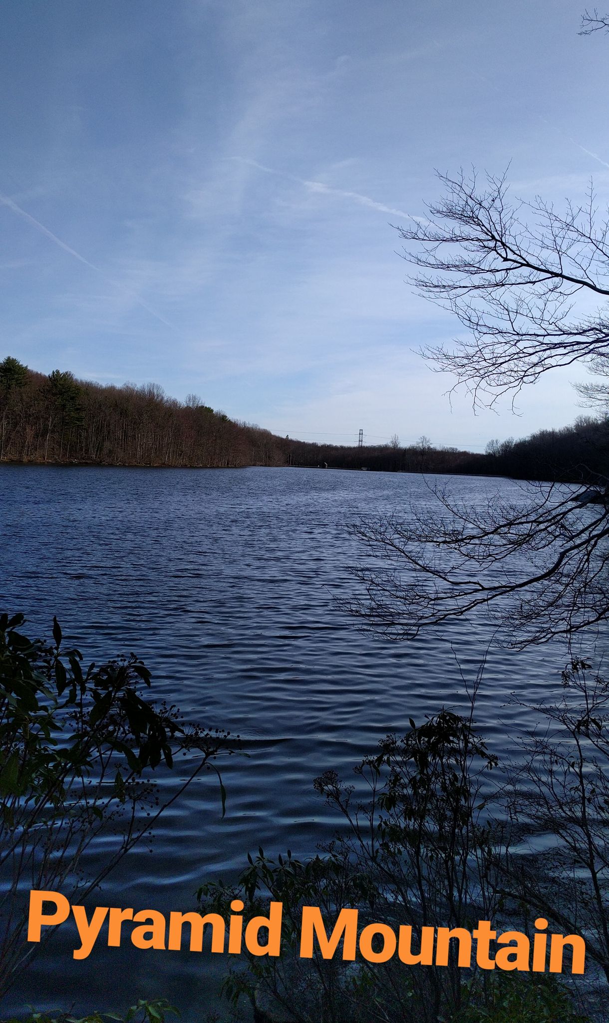Calm lake surrounded by bare trees and forested hills under a bright blue sky. - Pyramid Mountain Natural Historic Area Green, Orange, and Blue Trails