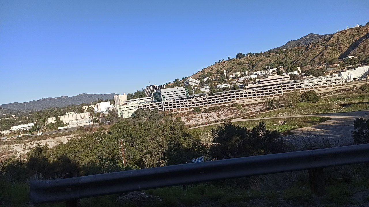 Large buildings and parking structures built into a dry hillside under a clear sky. - Devil's Gate Dam loop from Altadena