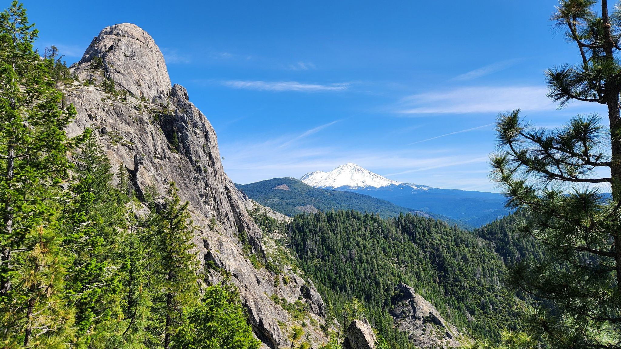Sunny view of a large rock formation, forested mountains, and a distant snow-capped peak. - Crags Trail to Castle Dome