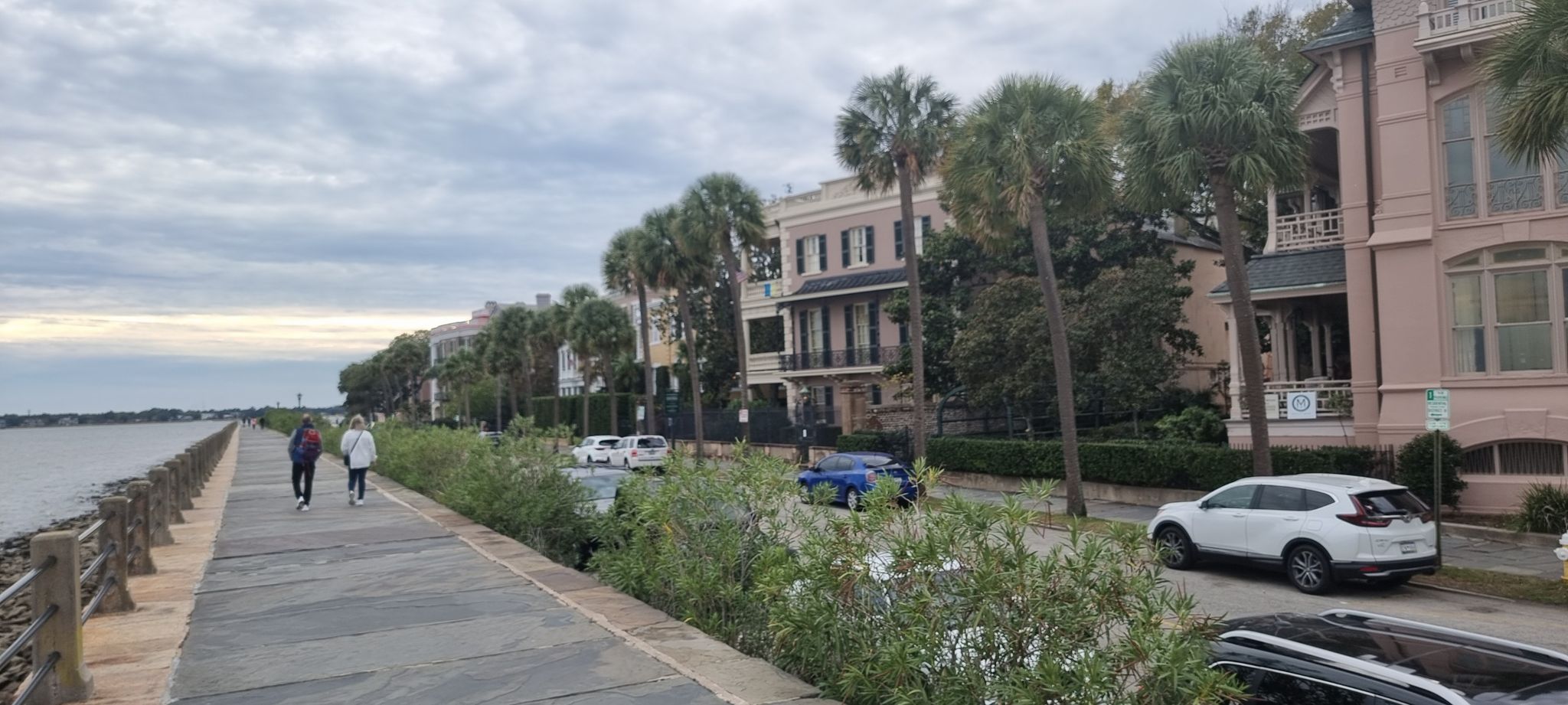 Two people walk on a waterfront promenade lined with buildings and palm trees. - Downtown/Park Circle loop