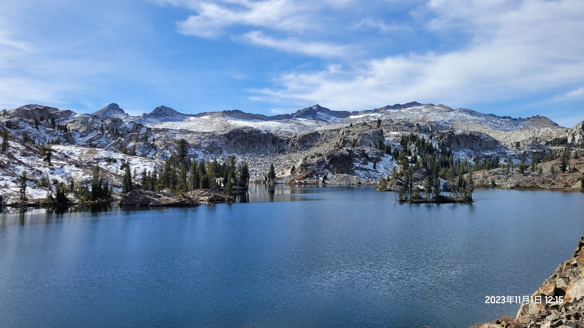 Panoramic view of a blue lake with snowy mountains and small forested islands. - Glen Alpine Trail to Clyde Lake