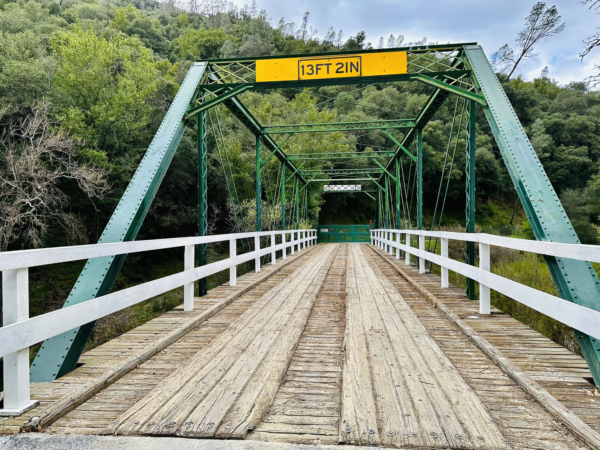 A green metal truss bridge with a wooden deck, surrounded by trees. - Old Gilroy Street – Historic Downtown Gilroy loop from Gilroy
