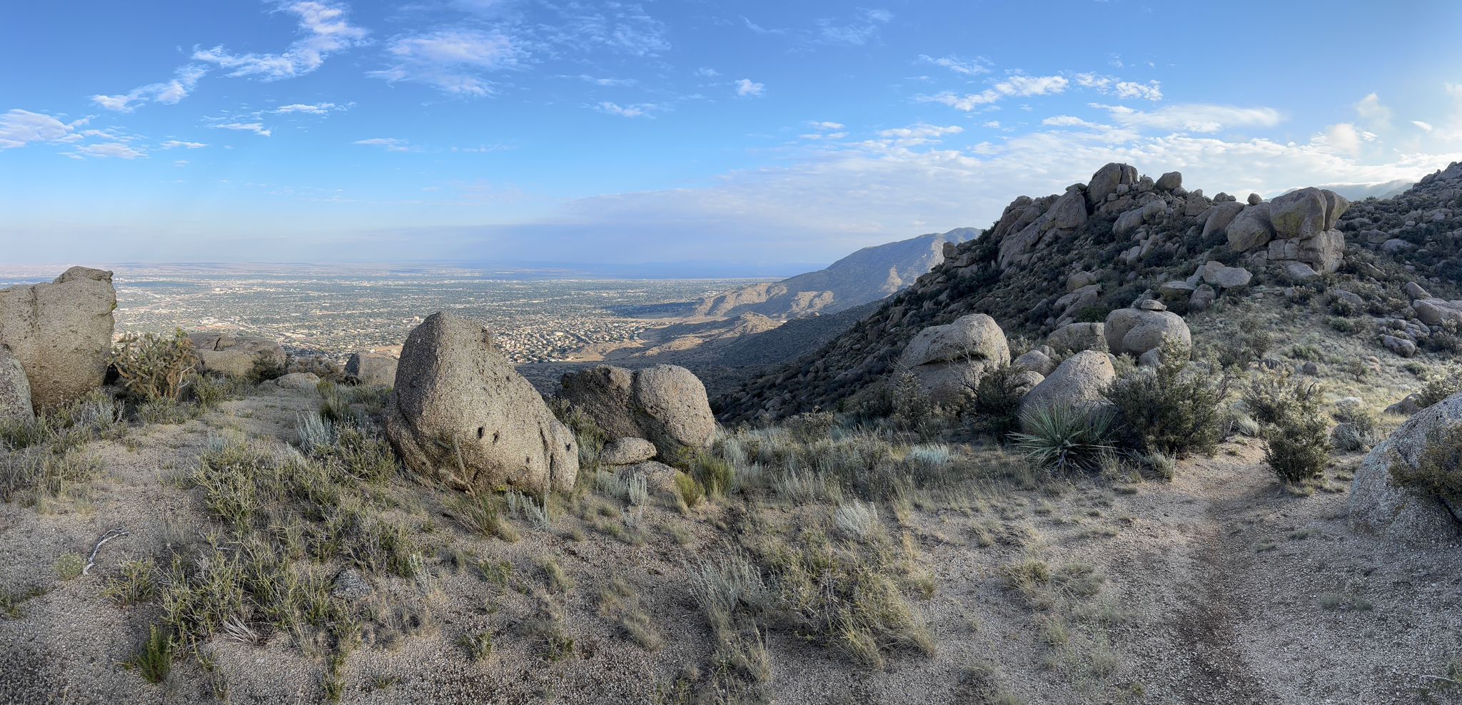 Panoramic view of a rocky desert landscape with distant city under blue sky. - Eye of the Sandias Loop