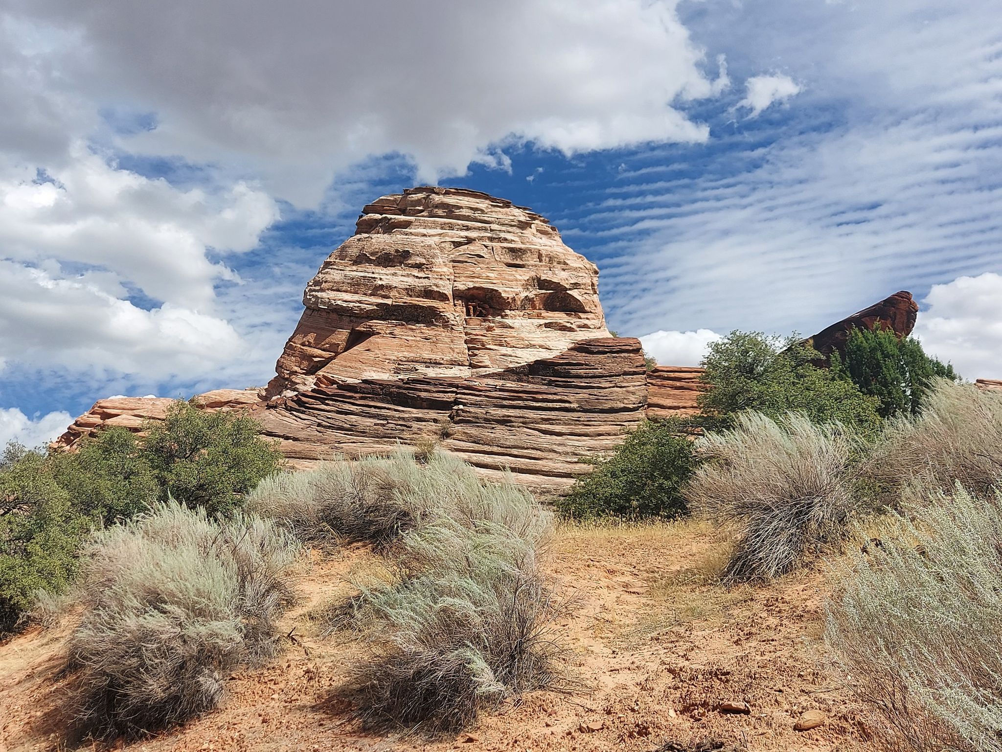 Layered red rock formation under a partly cloudy sky, surrounded by desert bushes. - Cottonwood Hills and Prospector Trail Loop