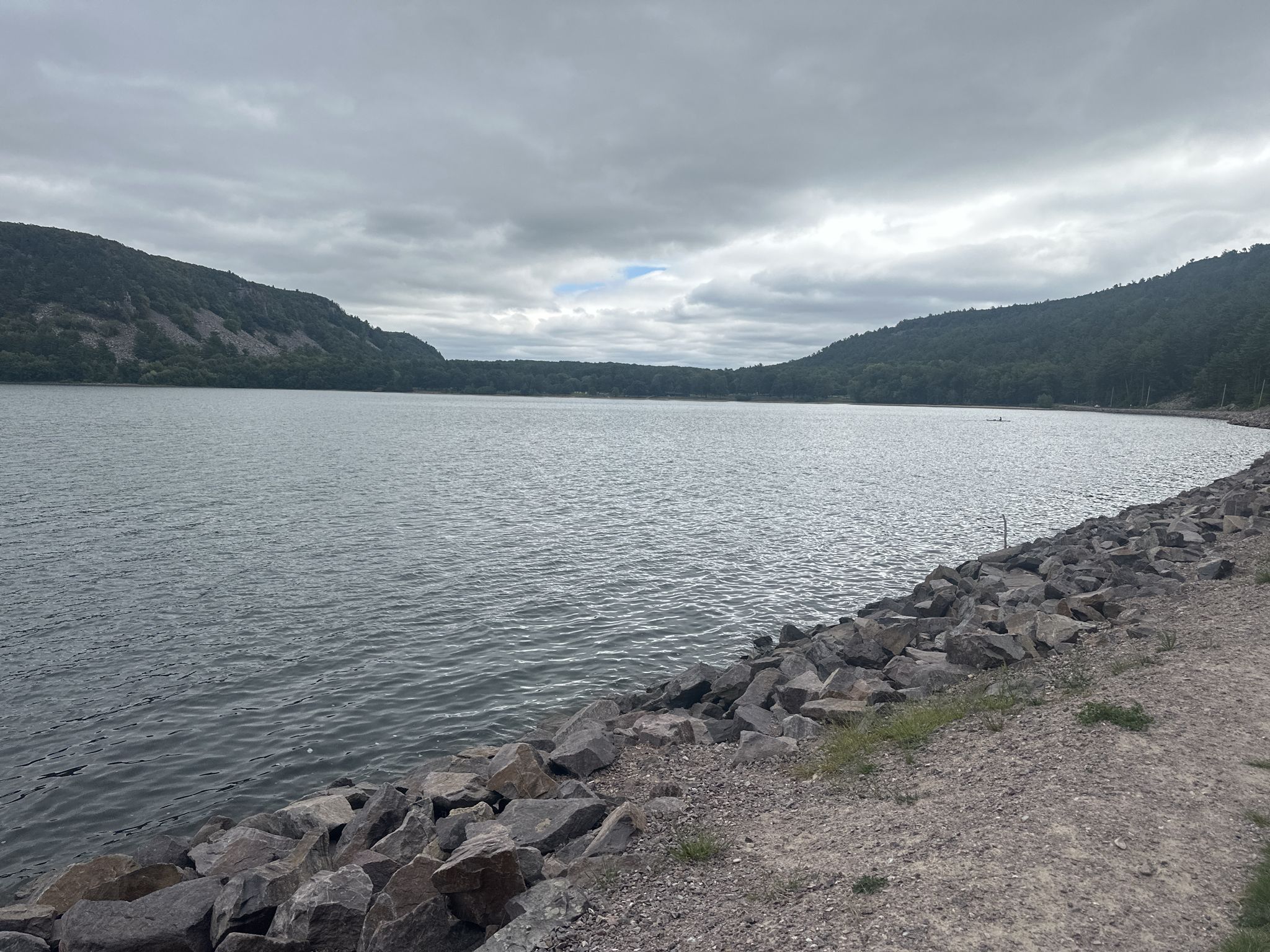 A wide lake with rocky shore, surrounded by forested hills under cloudy skies. - Devil's Lake State Park – Devil's Lake State Park loop from Baraboo