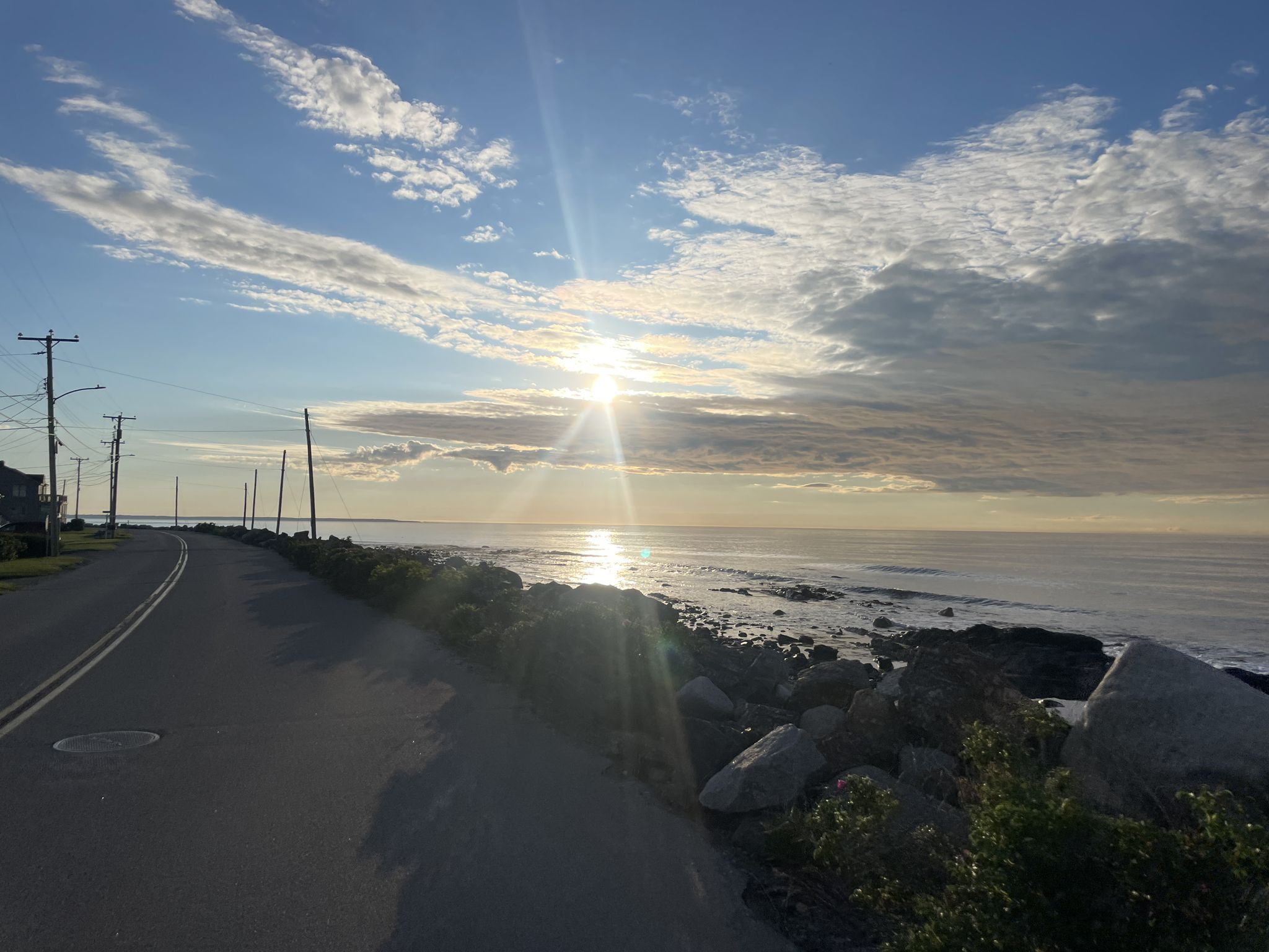 Sunburst over the ocean next to a coastal road with utility poles. - Moody Beach loop from Kennebunk