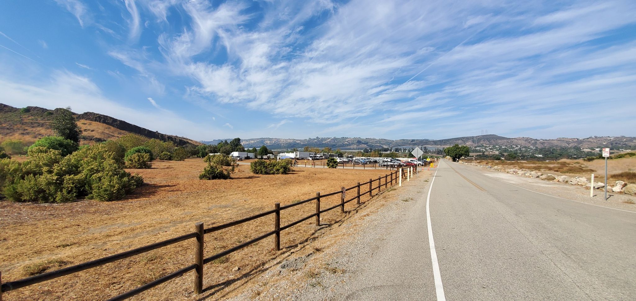 A paved road runs alongside a wooden fence in a dry, sunny landscape. - View from Western Plateau – Lizard Rock Bench loop from Wildwood Park