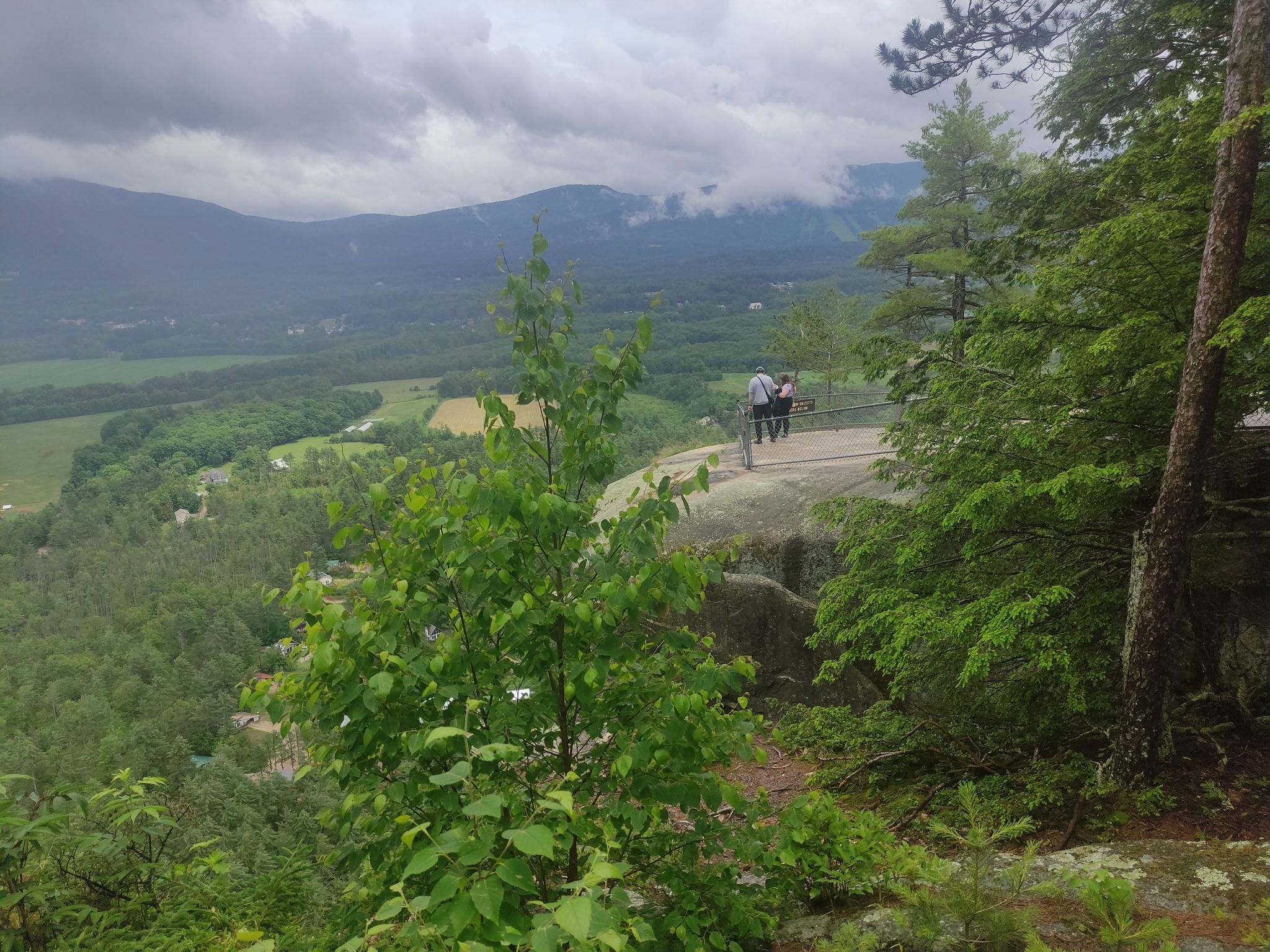 Two people on a rocky overlook viewing a cloudy, forested mountain valley. - Echo Lake, Cathedral Ledge, Whitehorse Ledge, and Diana's Baths