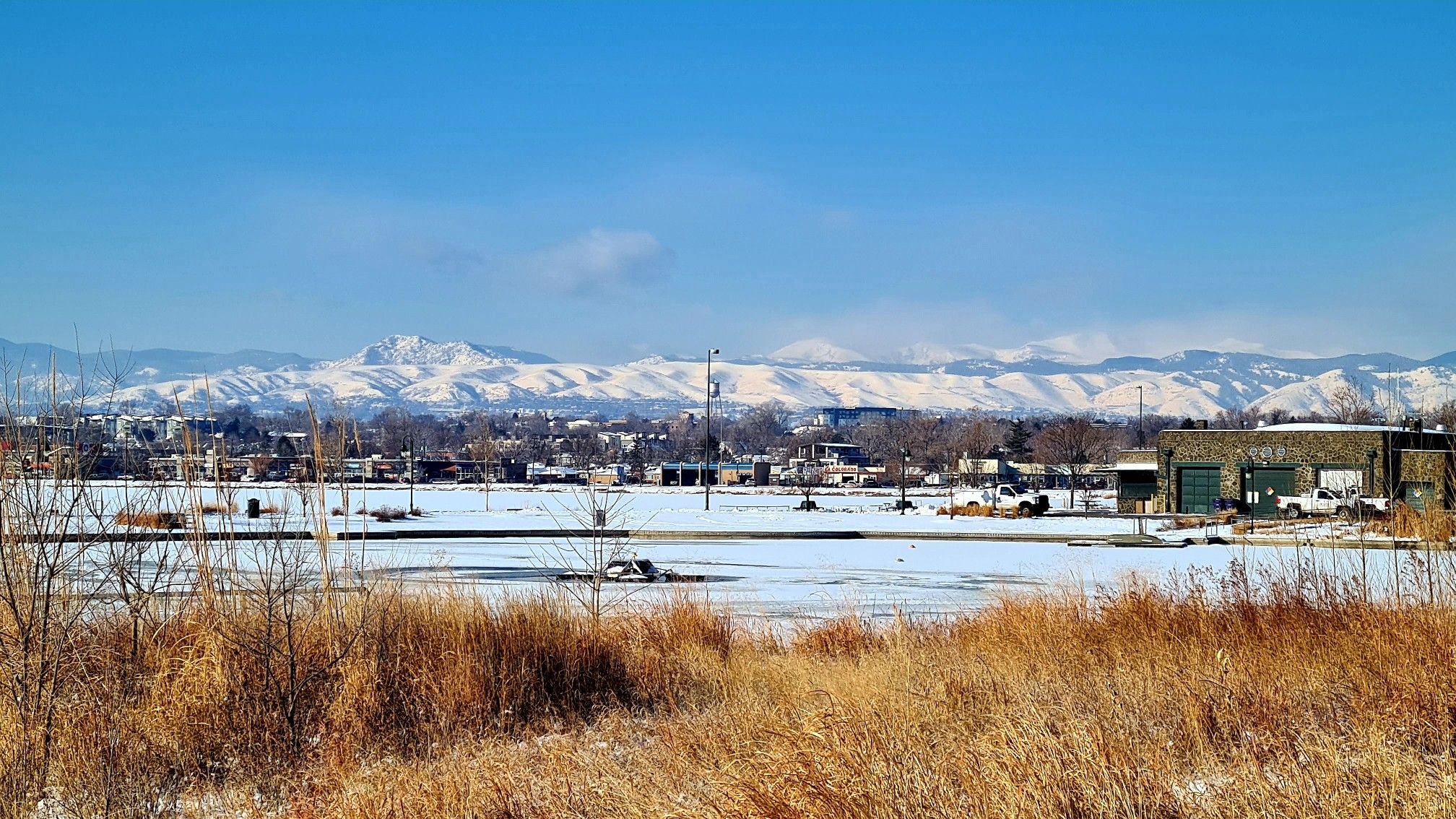 Snowy field with dry grass, distant mountains, and buildings under a clear sky. - Tucker Gulch – Lookout Mountain Climb loop from Knox