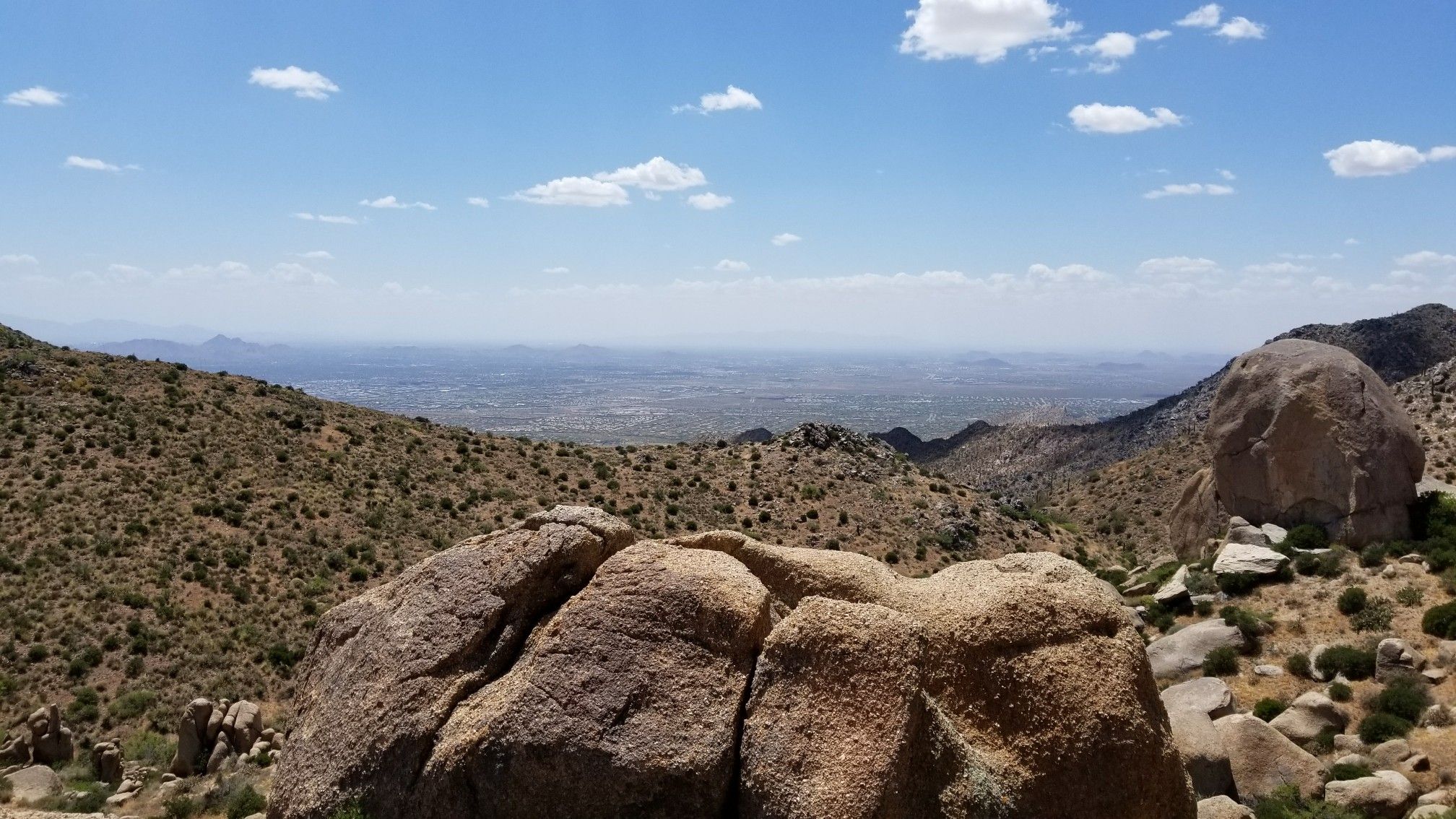 Sunny desert landscape with large boulders overlooking a distant city. - Tom's Thumb Trail