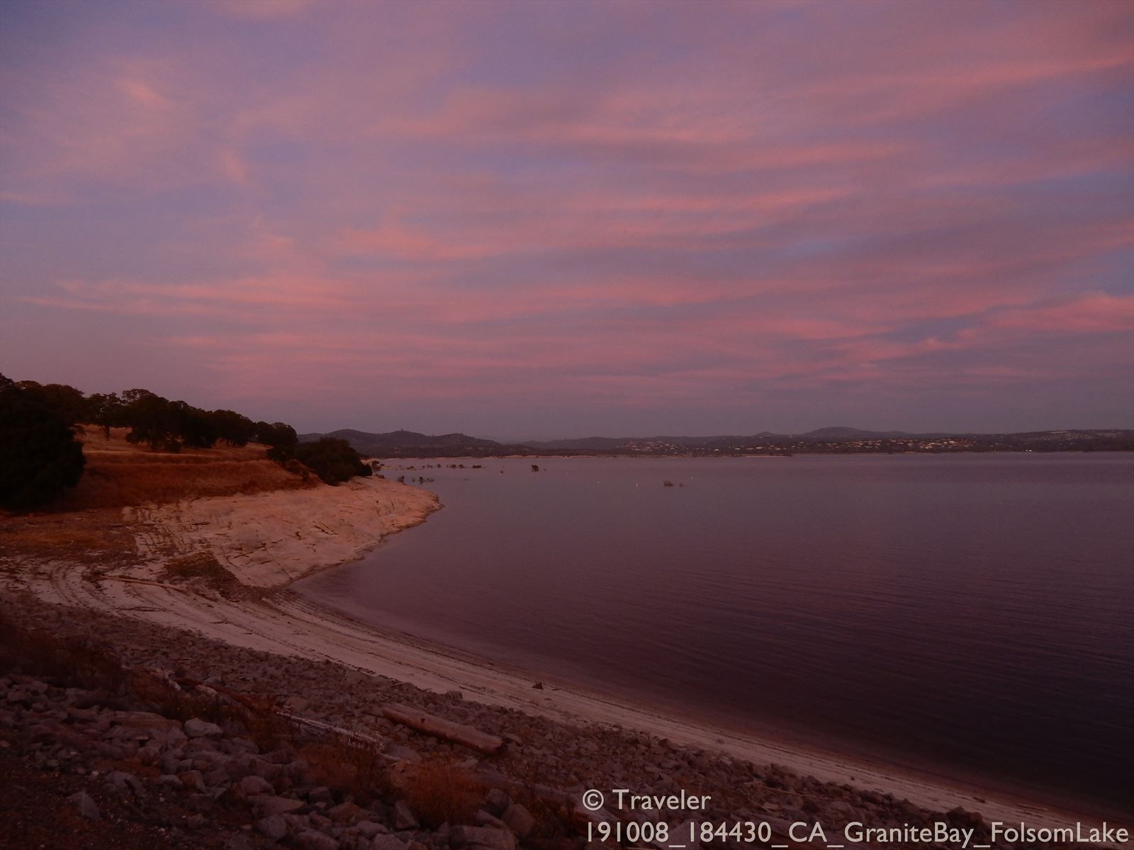 A lake at dusk with pink and purple clouds and a rocky shoreline. - American River Bike Trail: Beals Point Loop