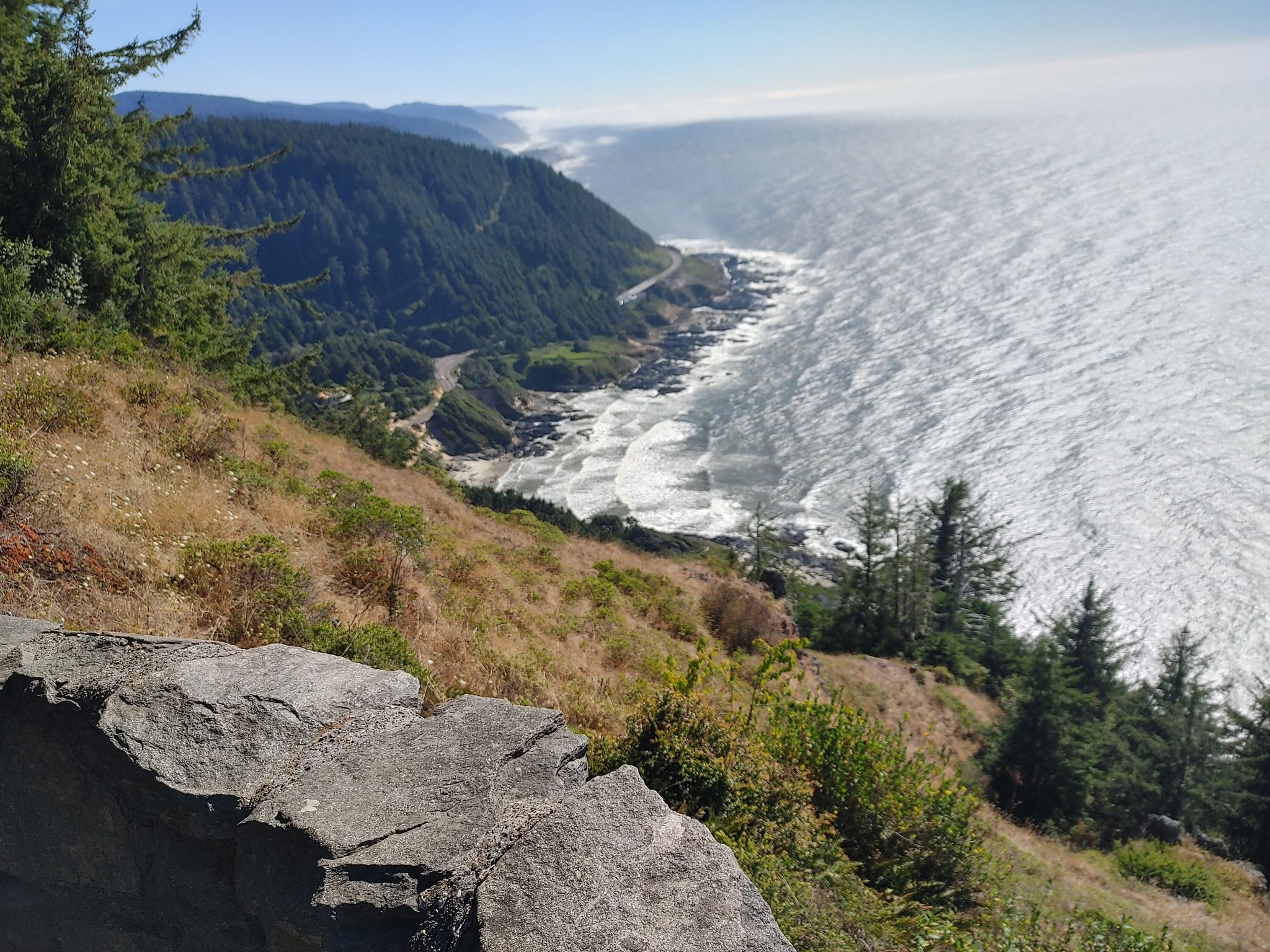 Panoramic view of a rugged coastline with ocean waves and a winding road. - Whispering Spruce Trail