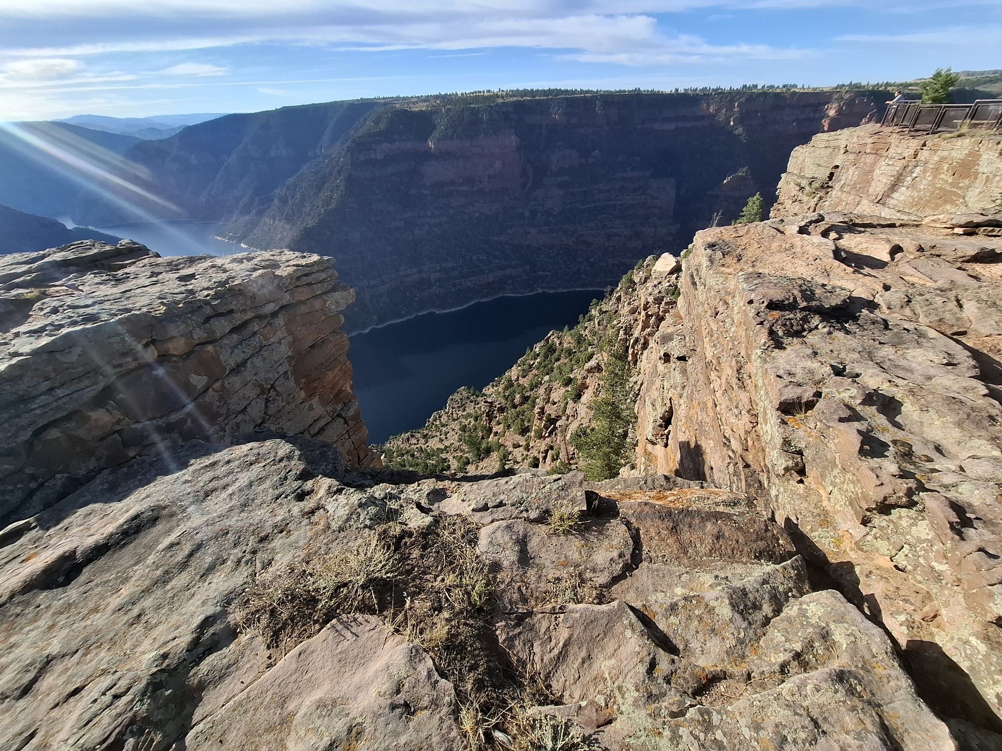 Sun rays illuminate a deep canyon with a winding river and rugged cliffs. - Red Canyon Rim Trail