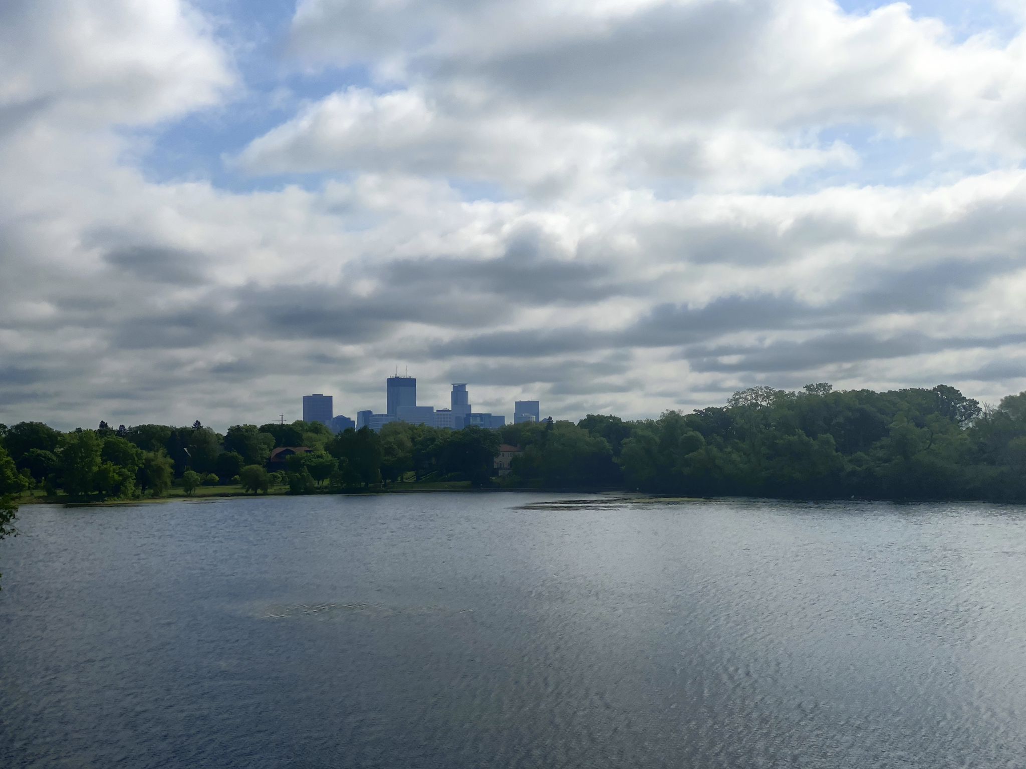 A city skyline visible across a wide lake with green trees. - Lake of the Isles – Midtown Greenway loop from Wooddale Avenue