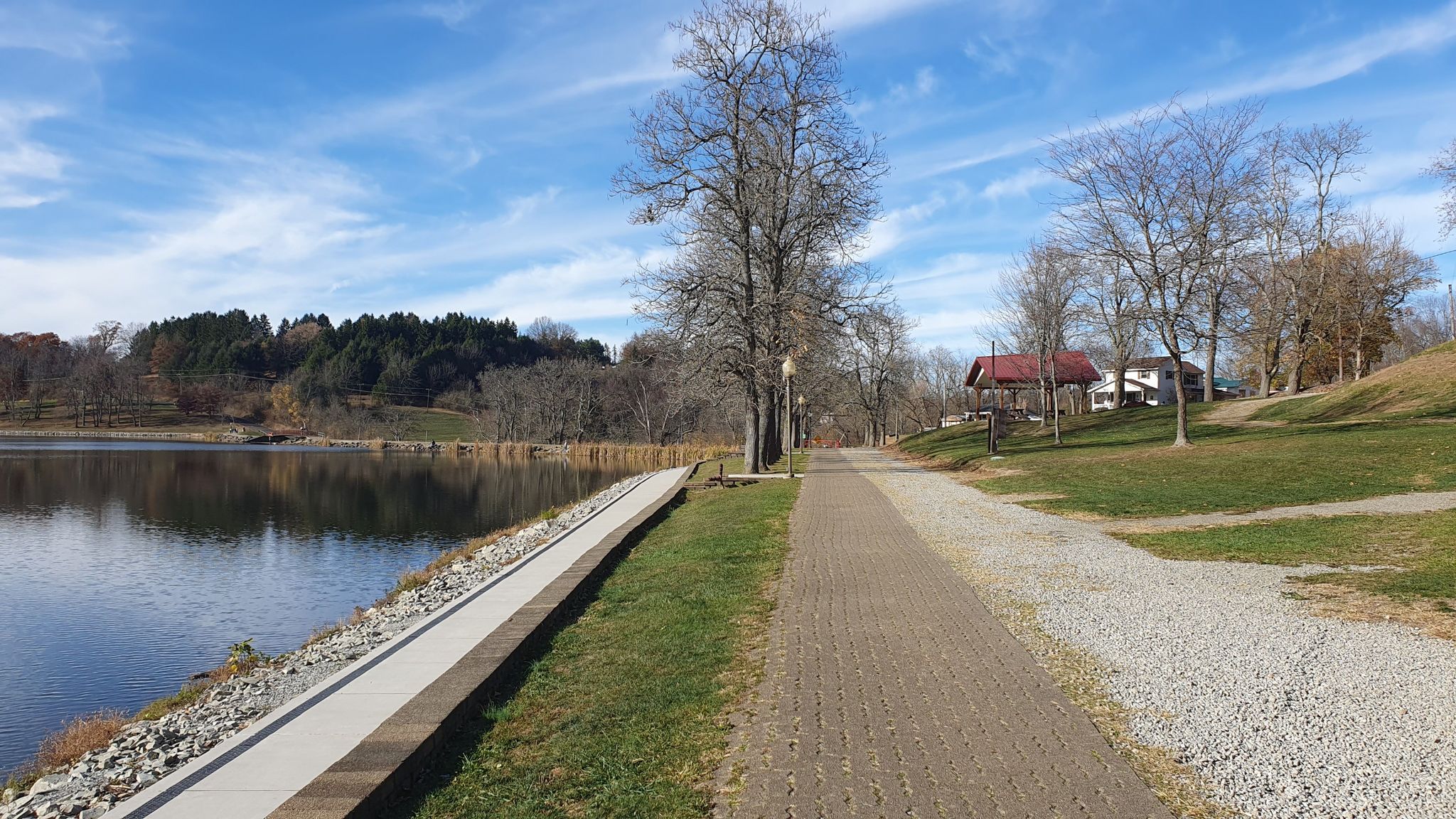 Calm lake beside paved and gravel paths, with bare trees and buildings. - Twin Lakes loop from Luxor
