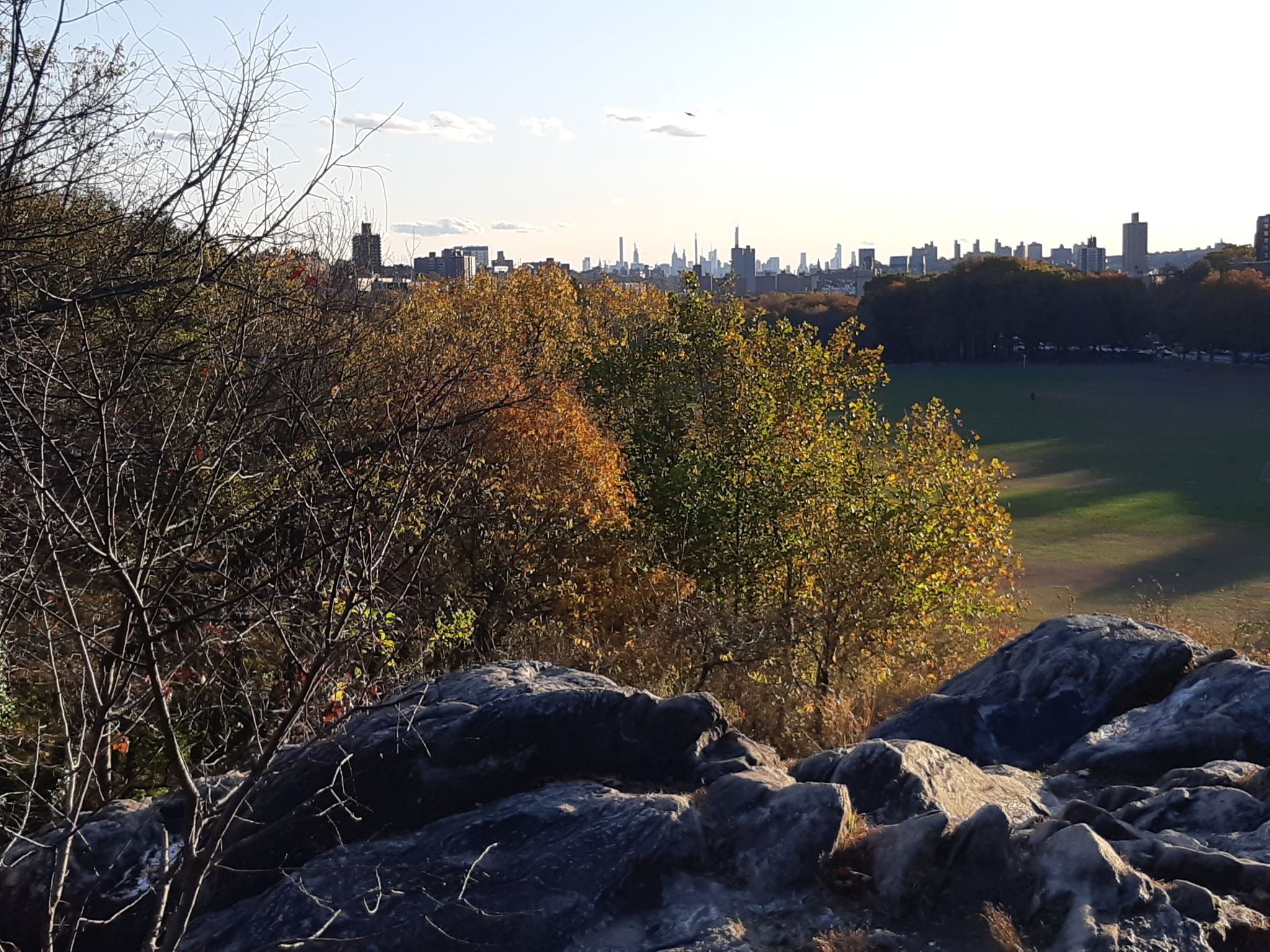 Rocky outcrop and autumn trees overlooking a distant city and large green field. - Cass Gallagher Nature Trail
