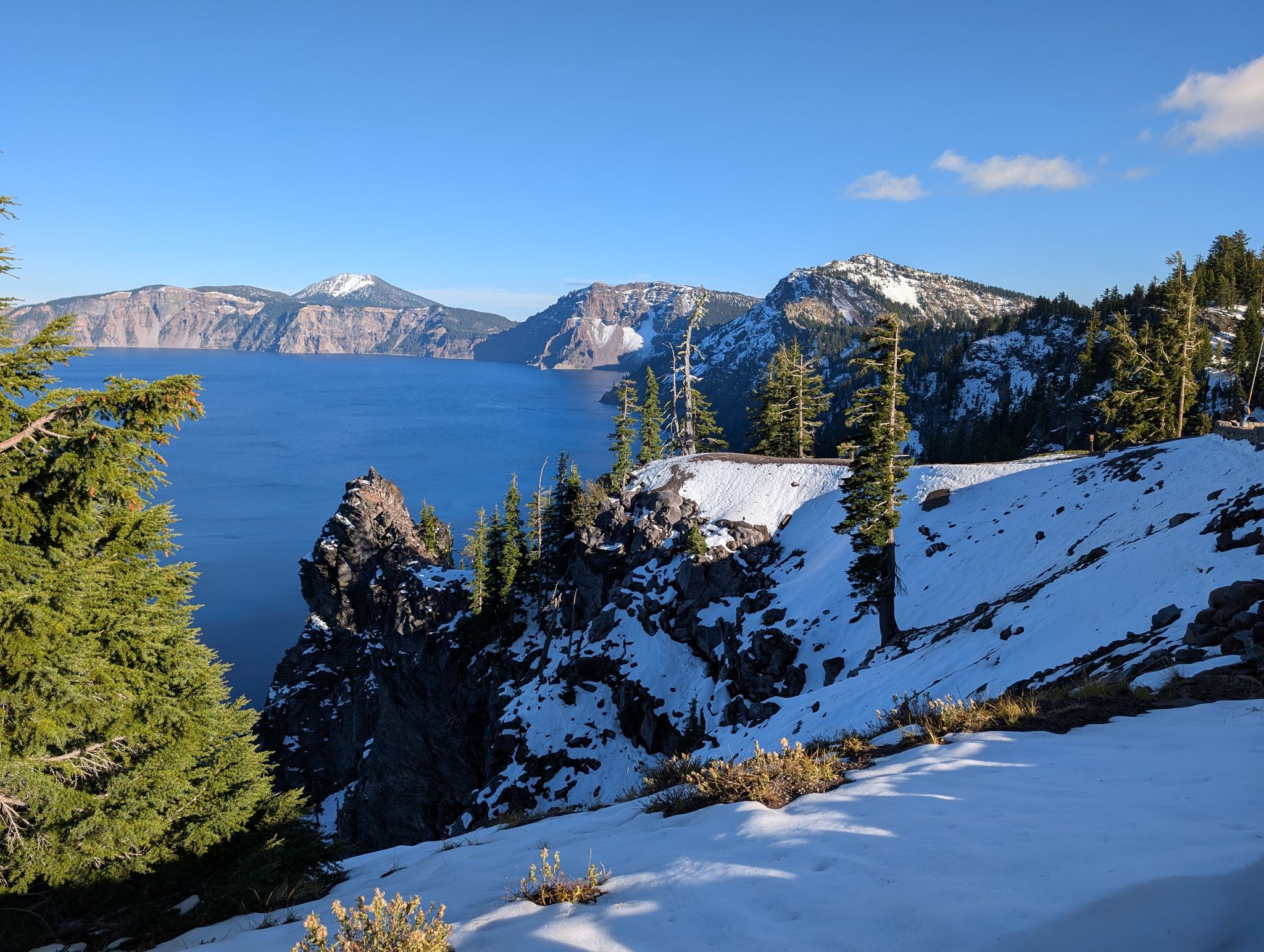 Snowy foreground with pine trees, overlooking a deep blue lake and distant mountains. - Rim Trail and Discovery Point Trail