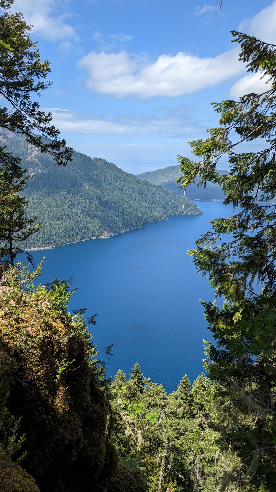 Bright blue lake framed by green trees and mossy rocks on a sunny day. - Mount Storm King Trail