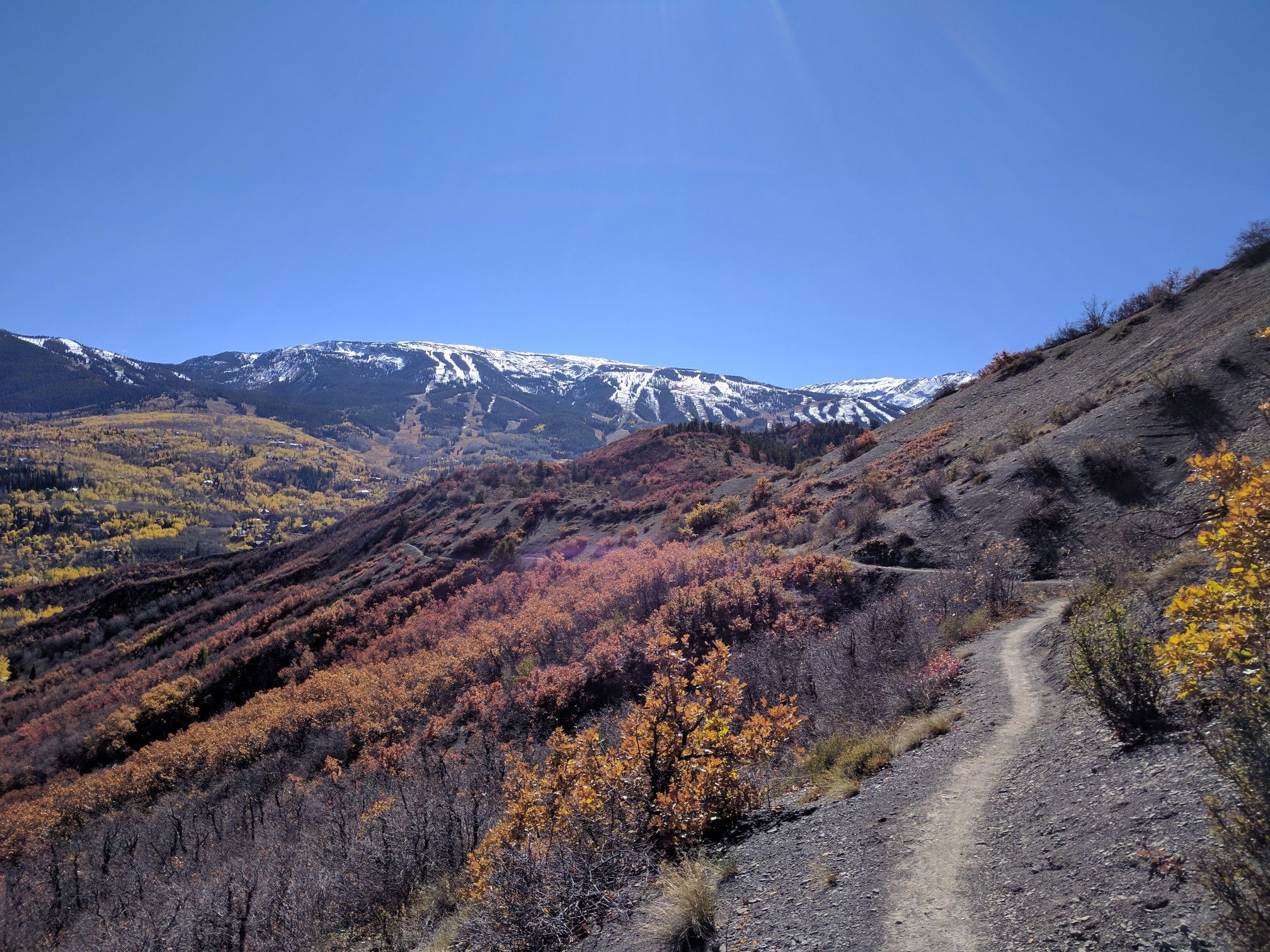 A dirt trail winds through autumn-colored hills towards snow-capped mountains. - Rim Trail loop