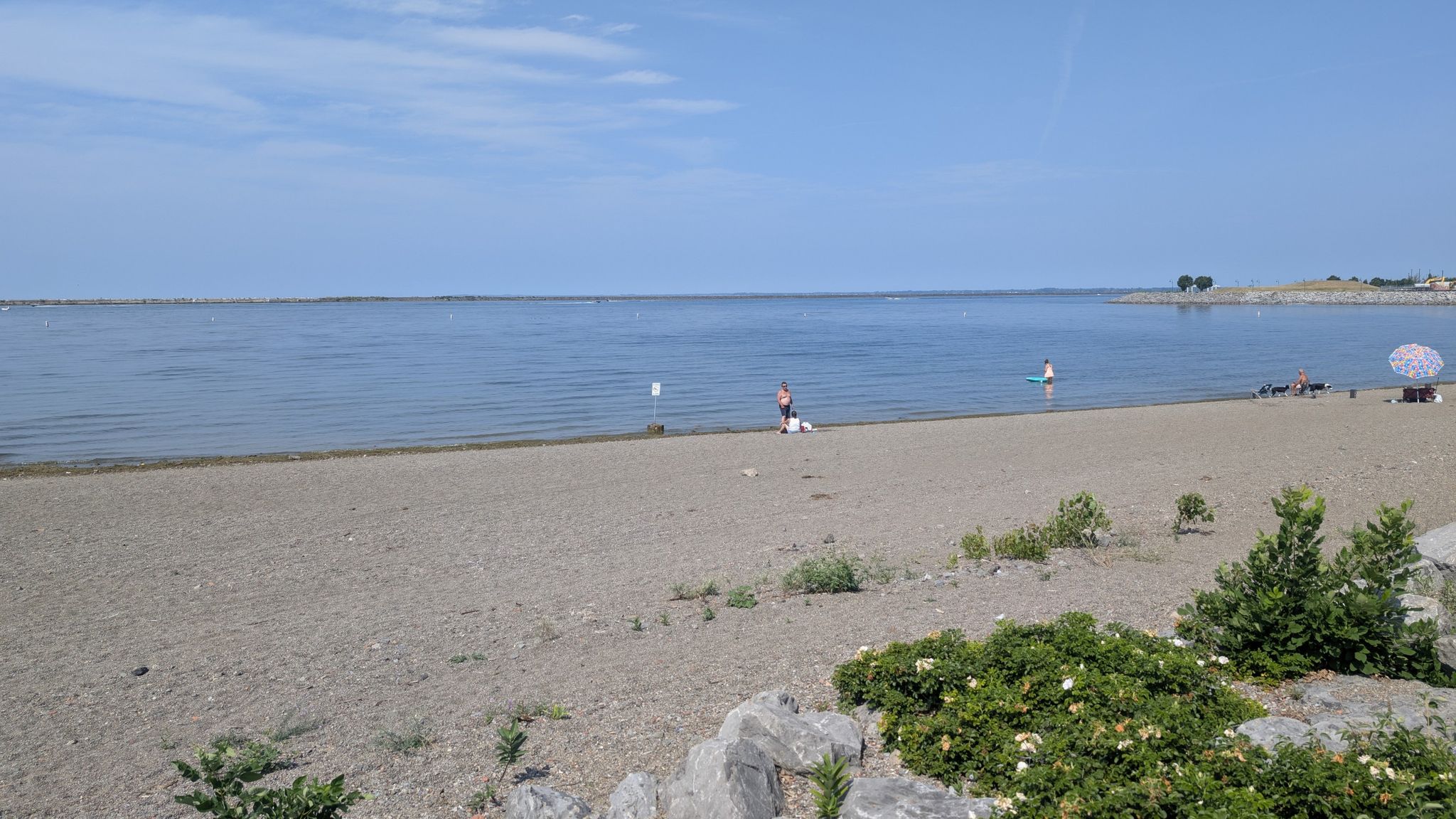 Sunny beach with calm water, few people, and green bushes. - New York Bike Route 517