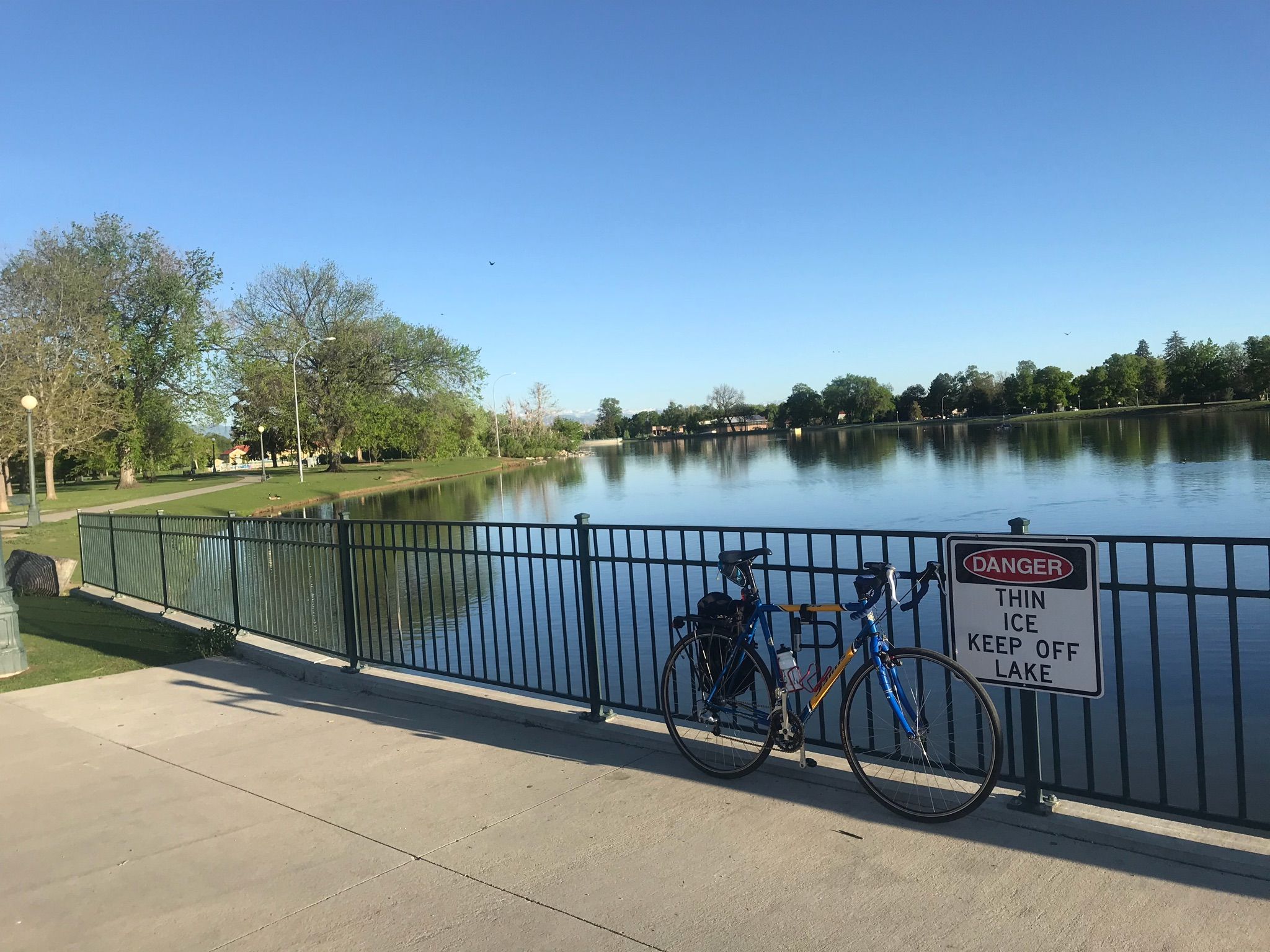 A bicycle parked next to a lake fence with a 'Thin Ice' sign on a sunny day. - Denver City Park Perimeter Loop